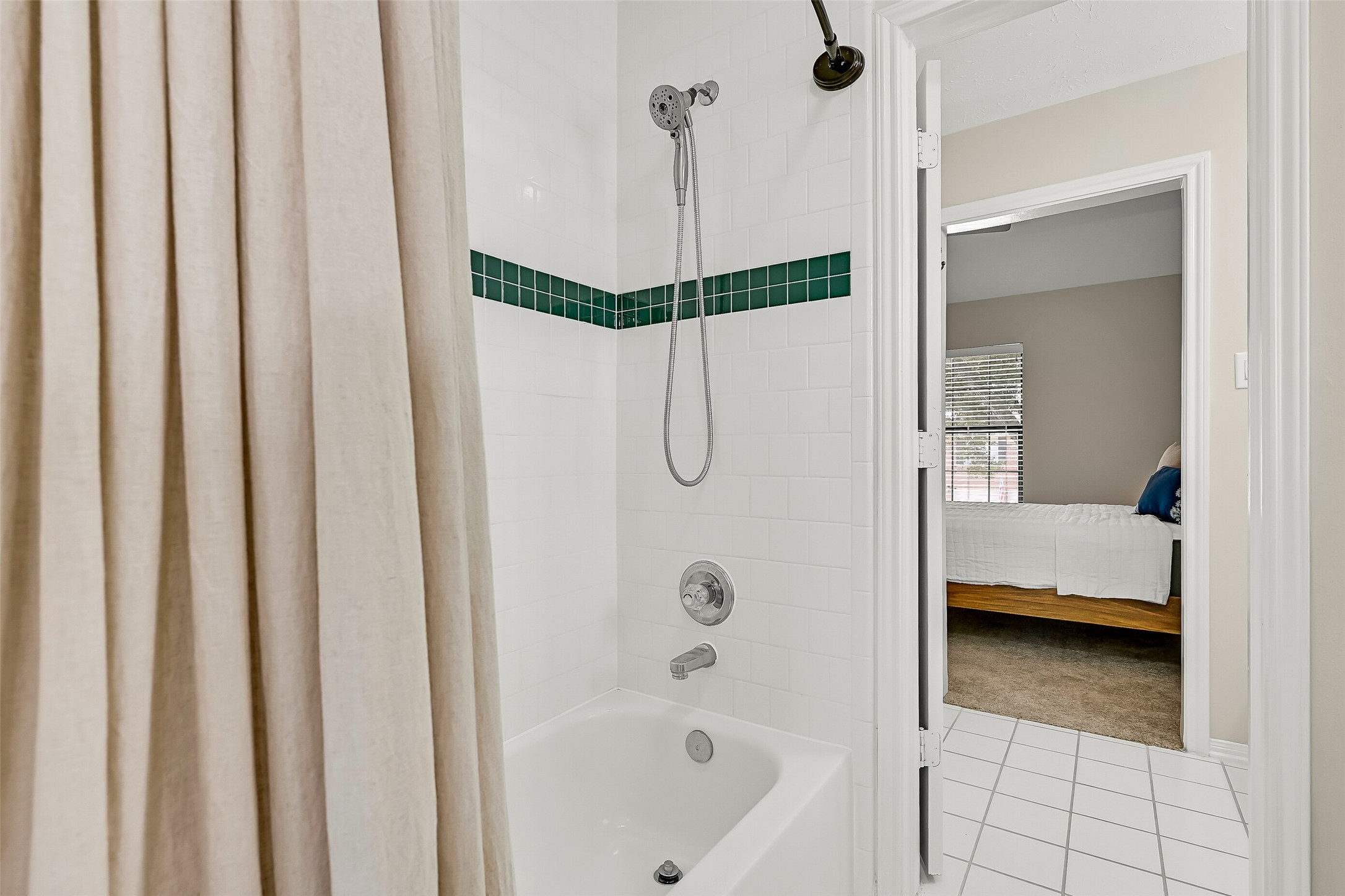 At the center of the Jack & Jill bath, a shared tub/shower features crisp white tile with a contrasting accent border, plus both fixed & handheld showerheads. Separate vanity areas on either side create an especially practical setup for the adjoining bedrooms.