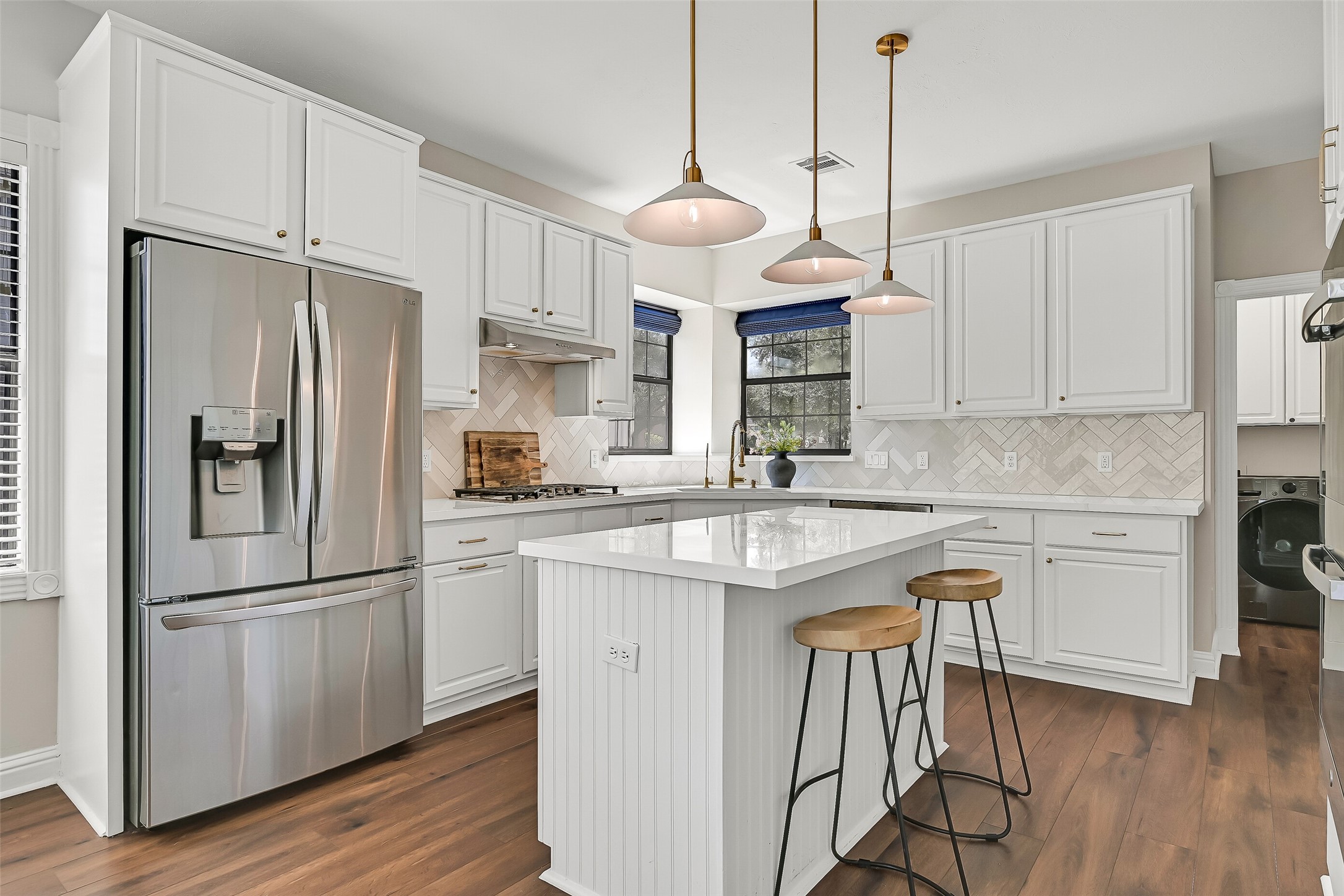 Bright and beautifully updated, the island kitchen features quartzite countertops, white soft-close cabinetry, gold-tone hardware, a herringbone tile backsplash and stainless steel appliances. The oversized island provides additional prep space, storage & casual seating.