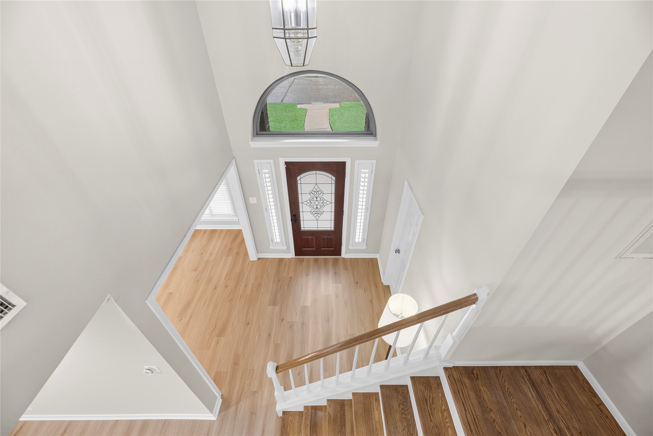 The foyer is just as impressive from the 2nd-floor landing, where soaring ceilings, fresh neutral paint, updated LVP flooring & an arched transom window create a bright, welcoming entrance below.