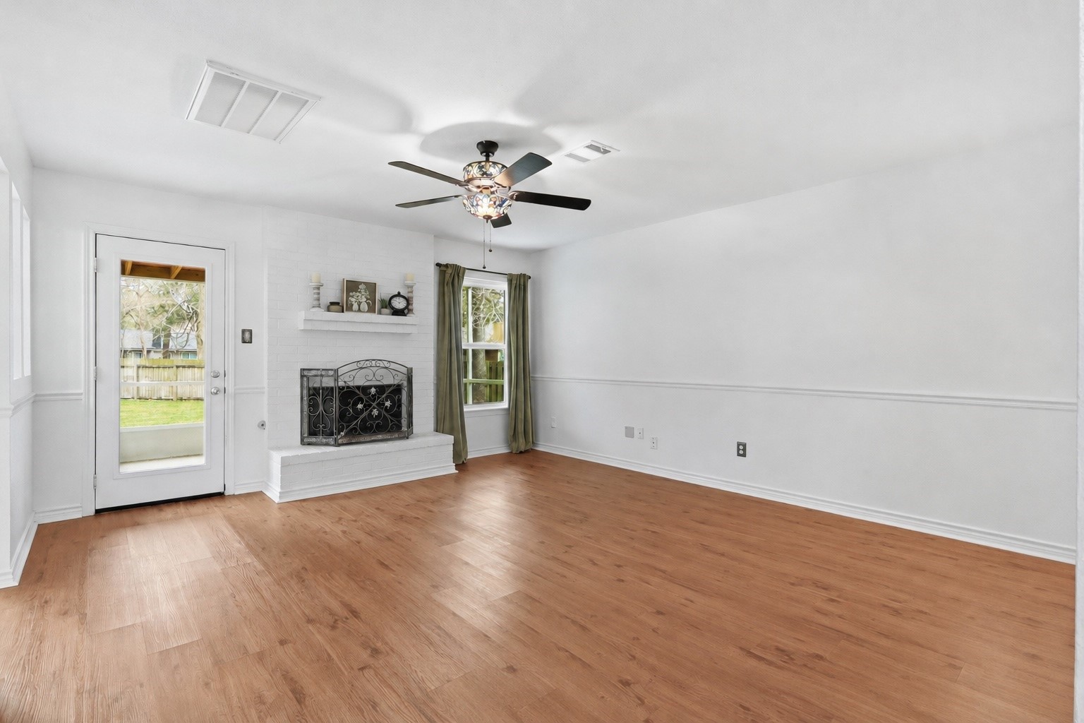 Spacious living room with brick fireplace and stained glass ceiling fan.