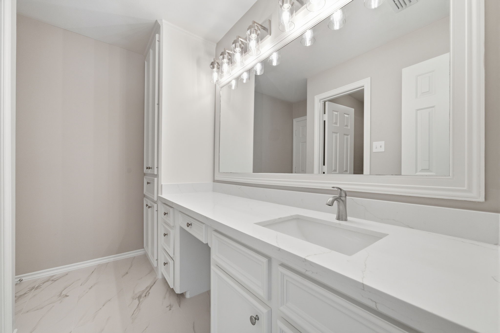Renovated bathroom showcases a large mirror that visually expands the room while updated flooring gives the space a fresh, clean appearance.