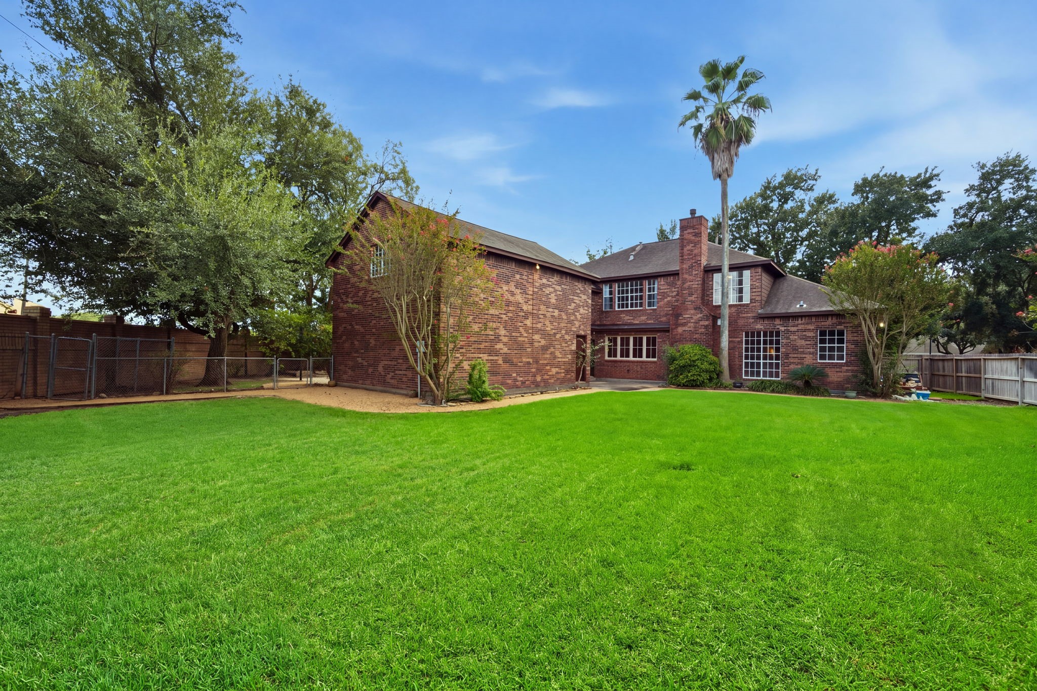 Spacious backyard with lush green lawn and mature trees, complementing a charming brick home perfect for outdoor activities and relaxation.