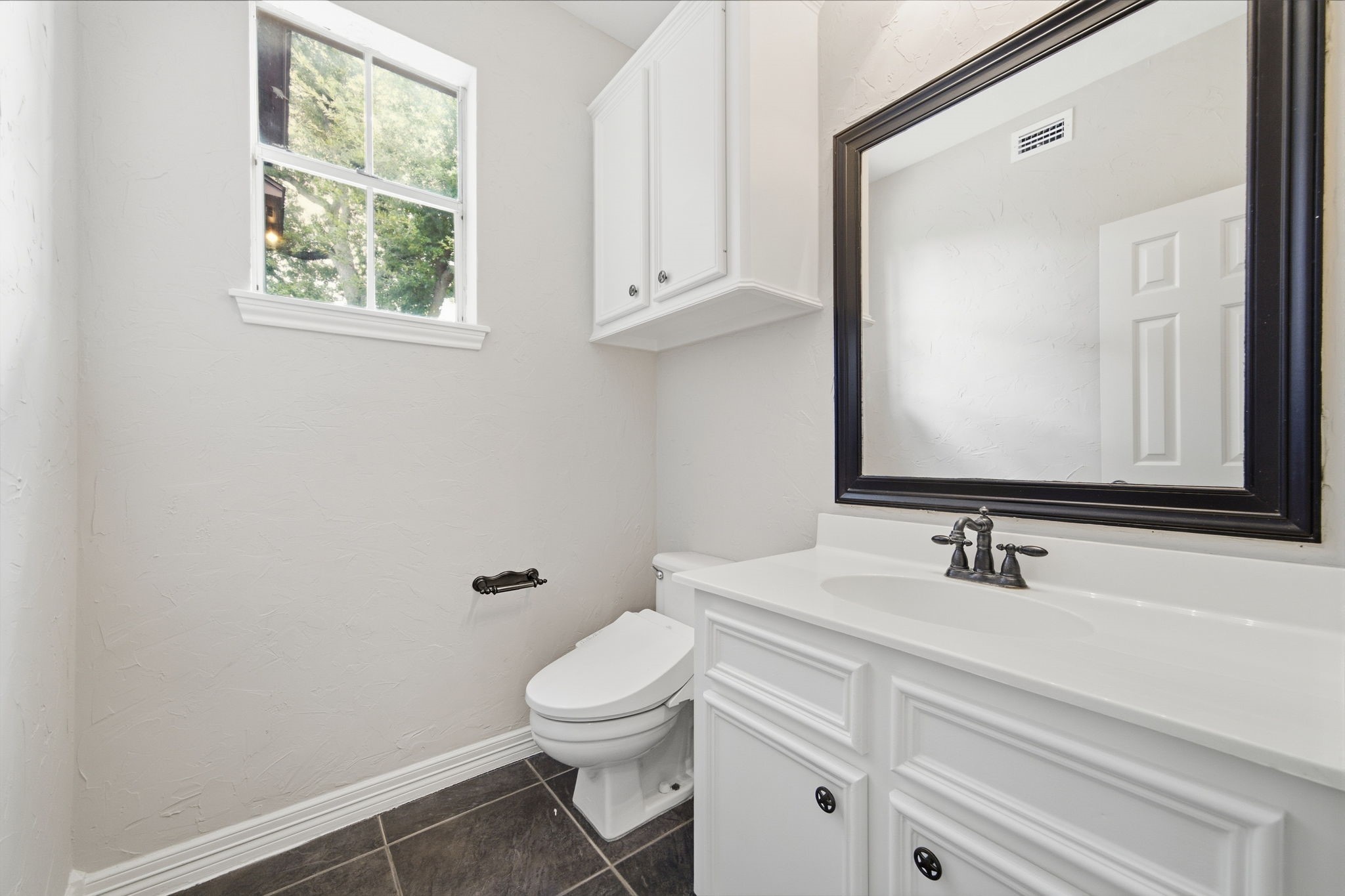 Bright guest bathroom with sleek tile flooring, a spacious vanity with a large framed mirror, and ample natural light from the window.
