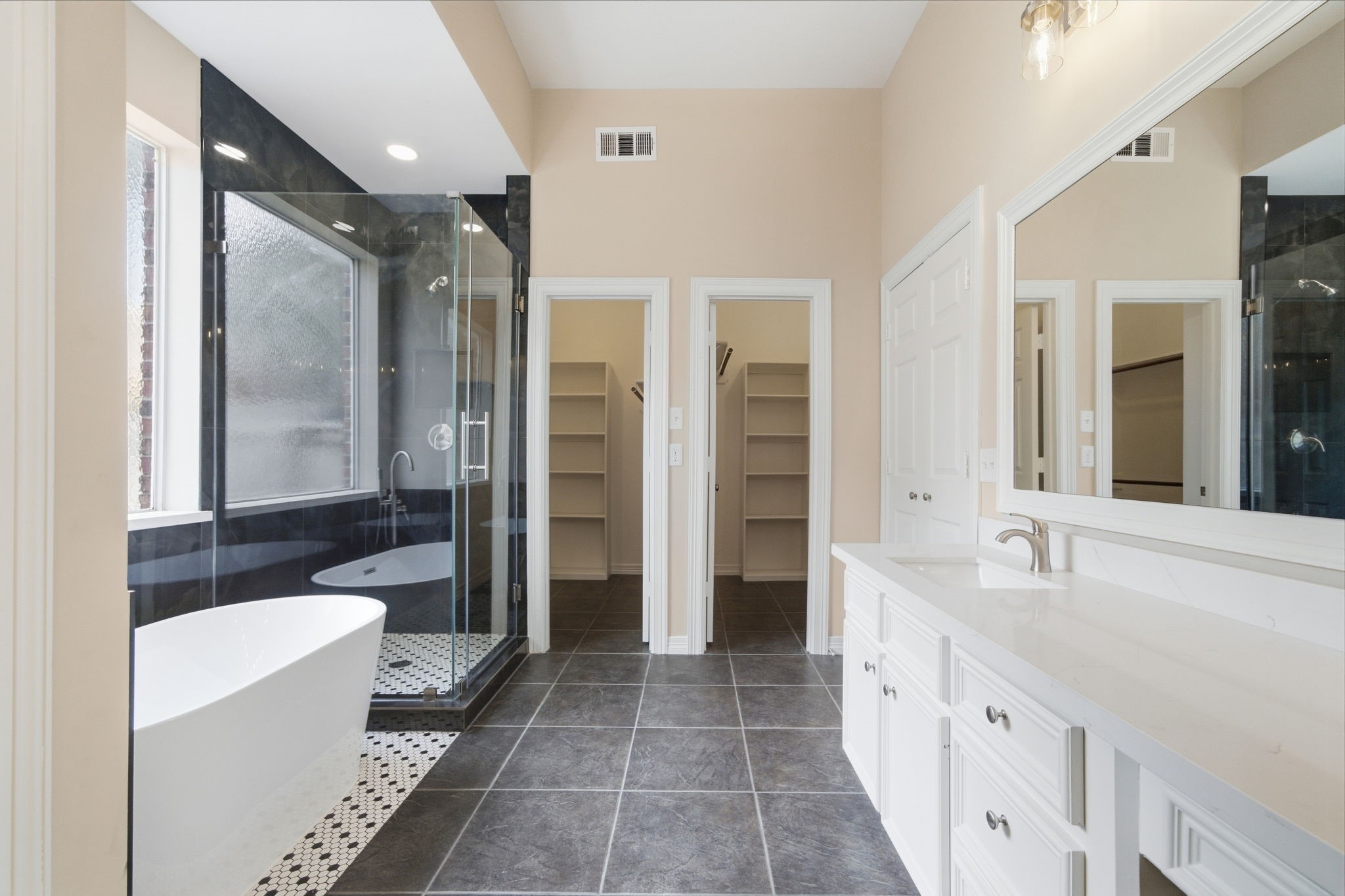 Luxurious bathroom featuring a sleek freestanding tub, a spacious glass-enclosed shower, dual vanities, and ample storage with 2 walk-in closets.