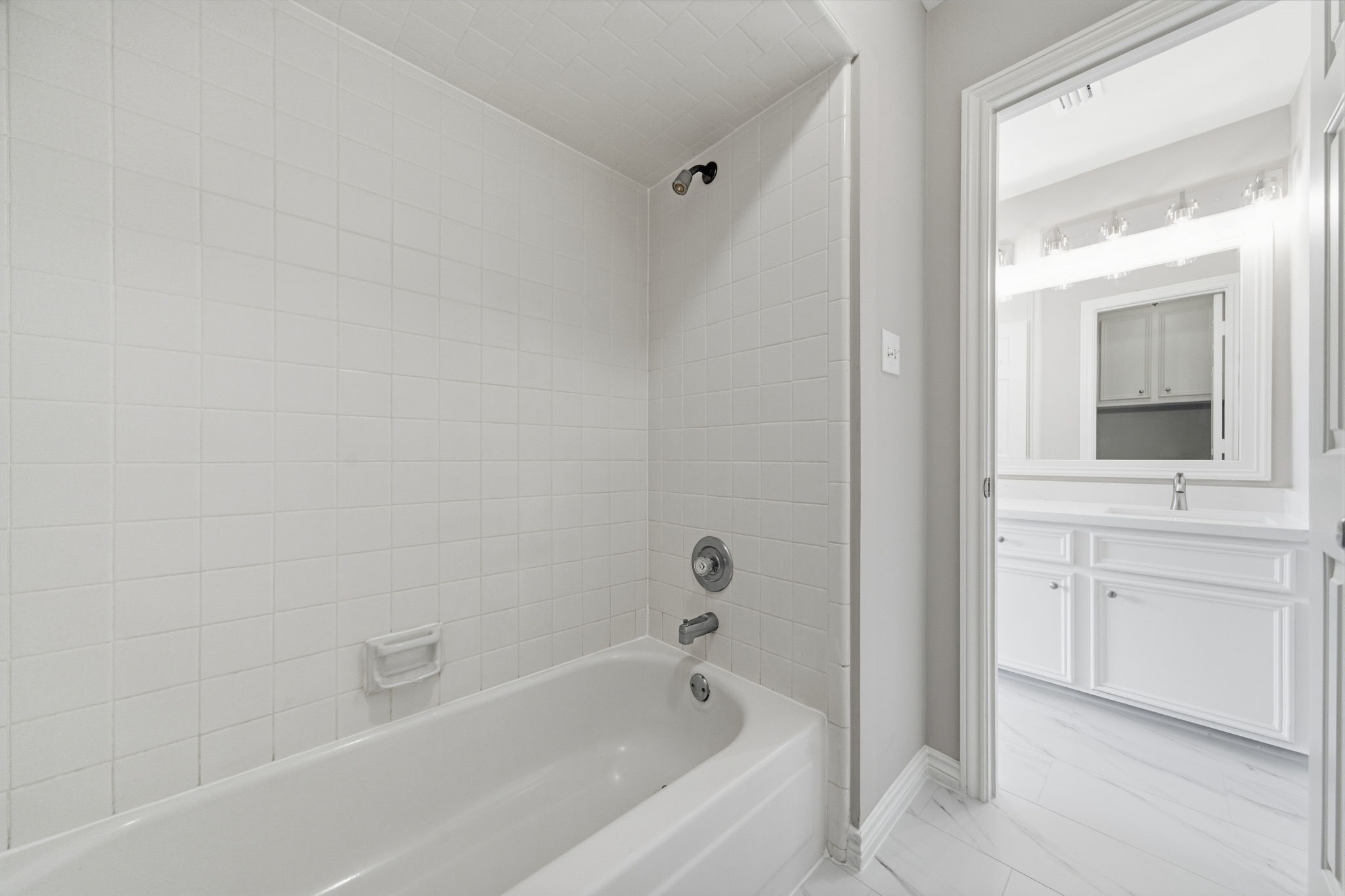 The secondary bath offers a bright vanity area with generous cabinetry and plenty of counter space for everyday routines. The adjoining tub and shower area is finished in classic white tile for a timeless look.