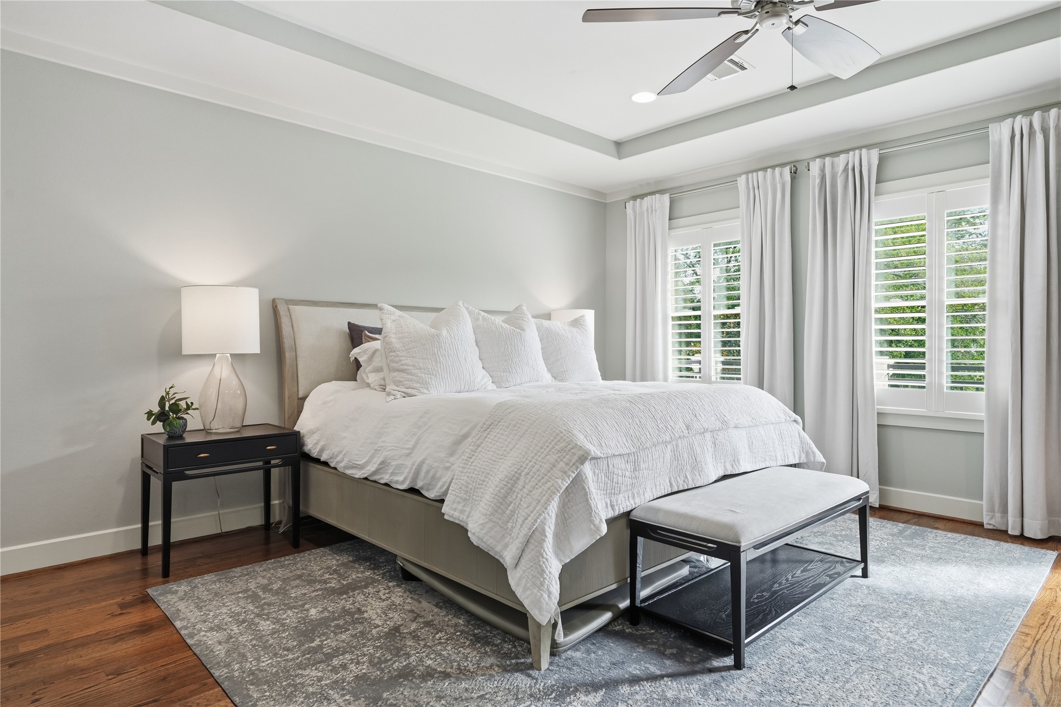 Retreat to the generously sized primary bedroom featuring hardwood floors, elegant tray ceilings, and abundant natural light throughout.
