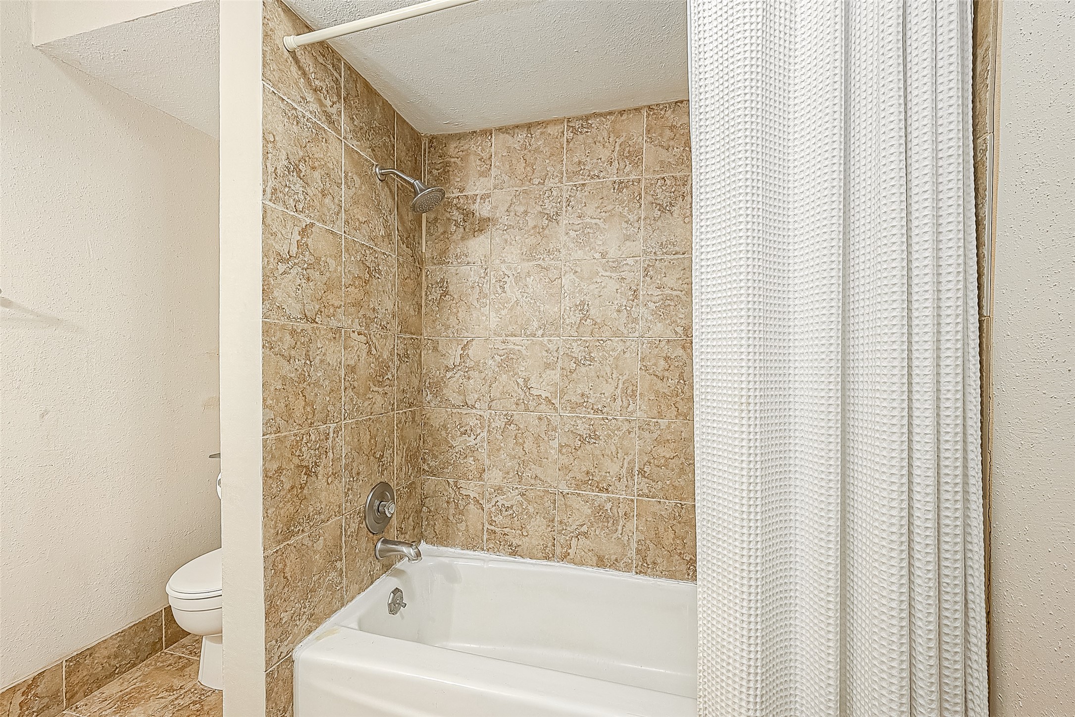 Bath features a tub/shower combination with tiled surround & coordinating tile flooring.