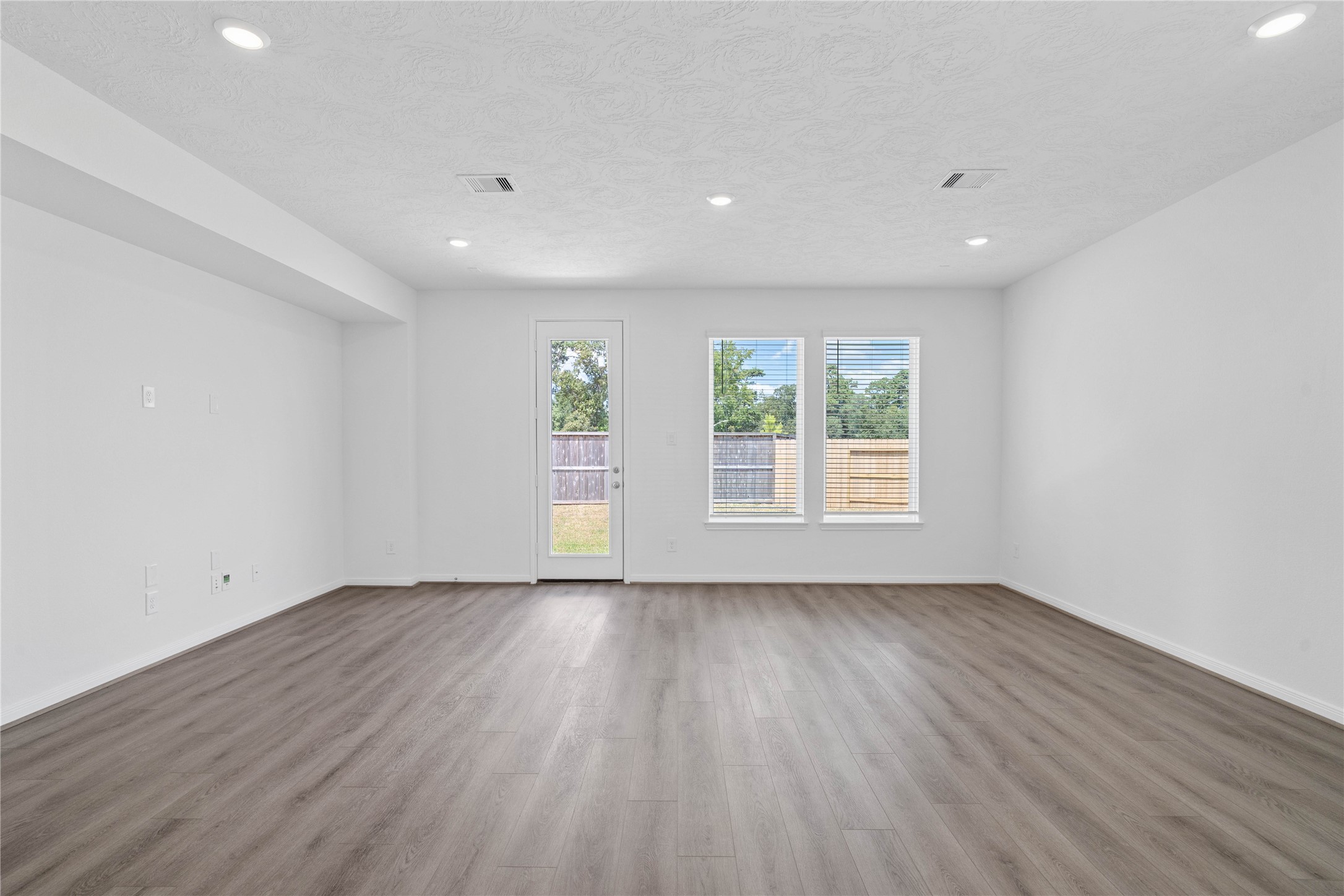 Bring family and friends together in this beautiful family room! It features high ceilings, recessed lighting, custom paint, stunning flooring, access door to the back patio, and large windows that fill the space with natural light all day long.