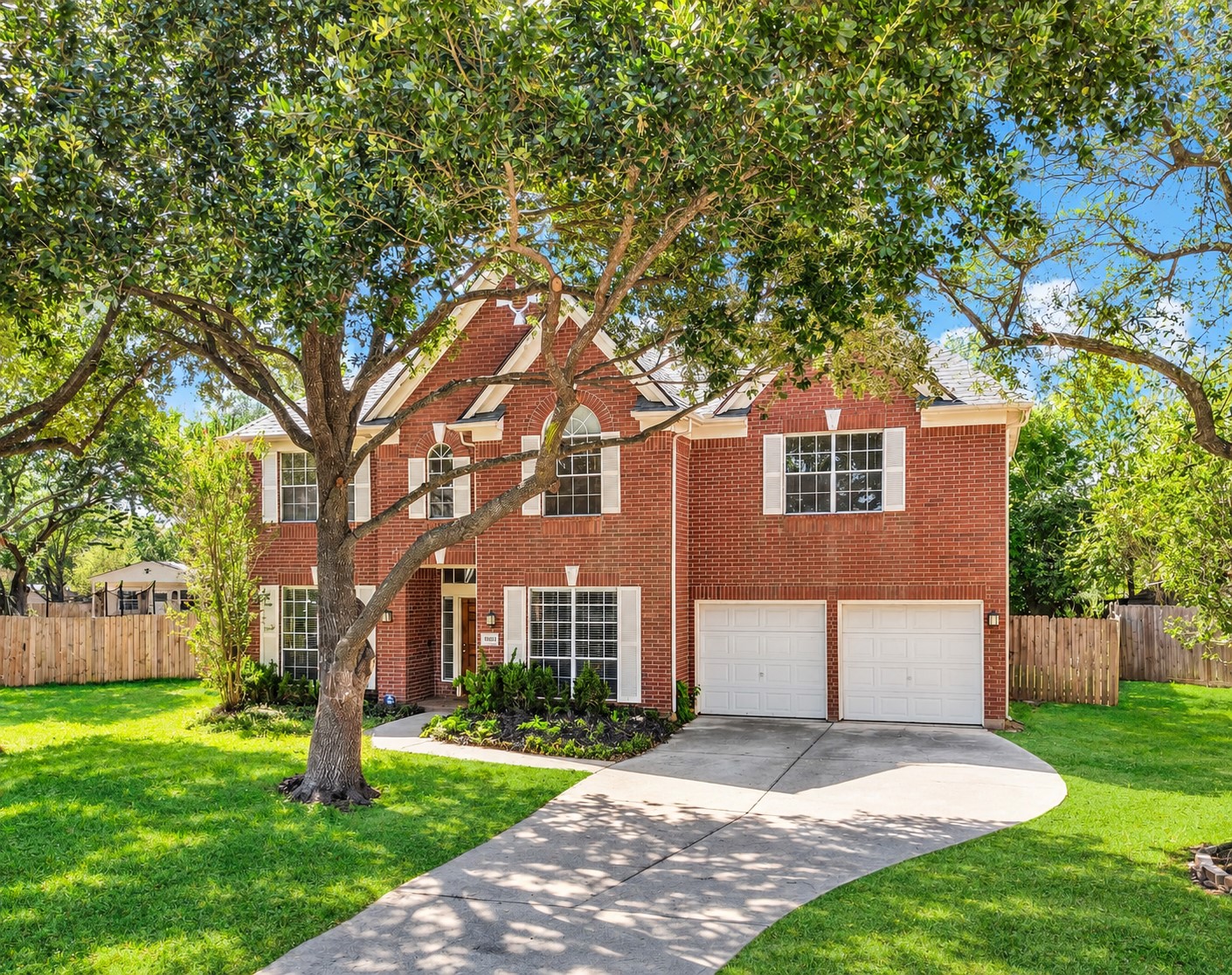 This view highlights the home's classic red brick exterior, attractive architectural details and beautifully framed windows, all beneath a canopy of mature trees.