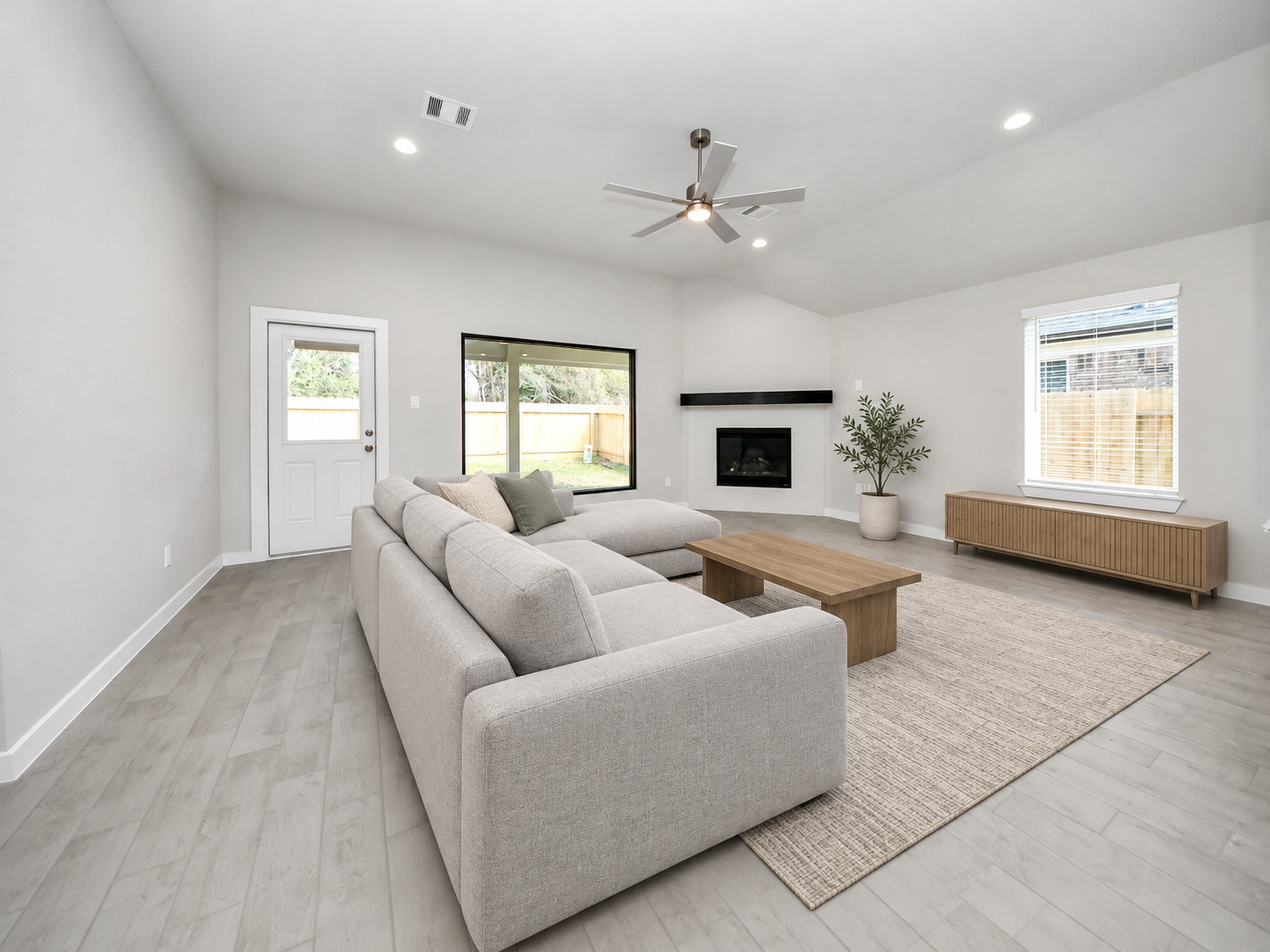 Spacious living room with modern gray flooring, large sectional sofa, and a sleek fireplace. Natural light pours in through a large window and glass door, enhancing the open and airy feel. Spacious living room with modern gray flooring, large sectional sofa, and a sleek fireplace. Natural light pours in through a large window and glass door, enhancing the open and airy feel.