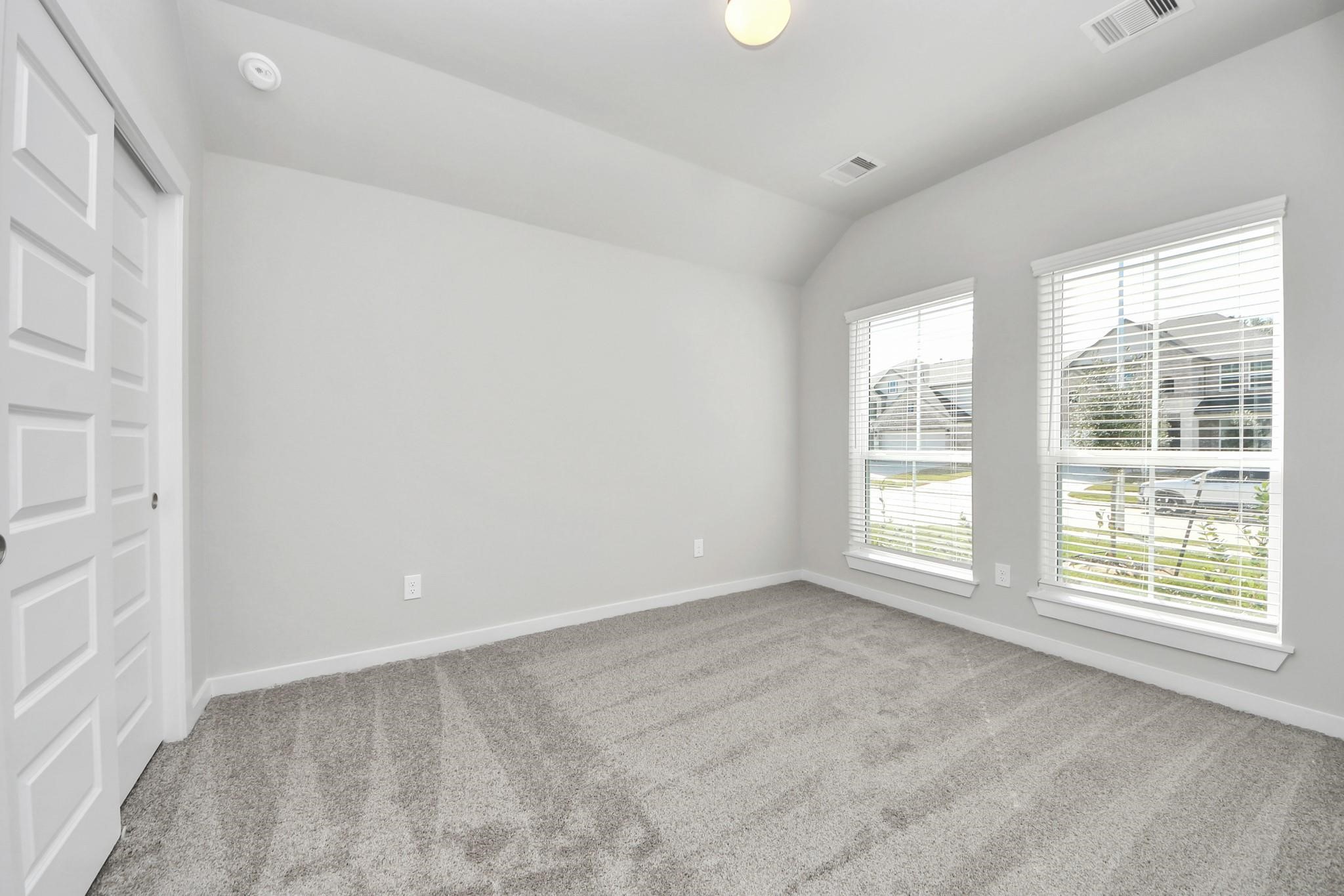 Bright and airy room with large windows, plush carpeting, and a spacious double-door closet, perfect for a cozy retreat or home office.