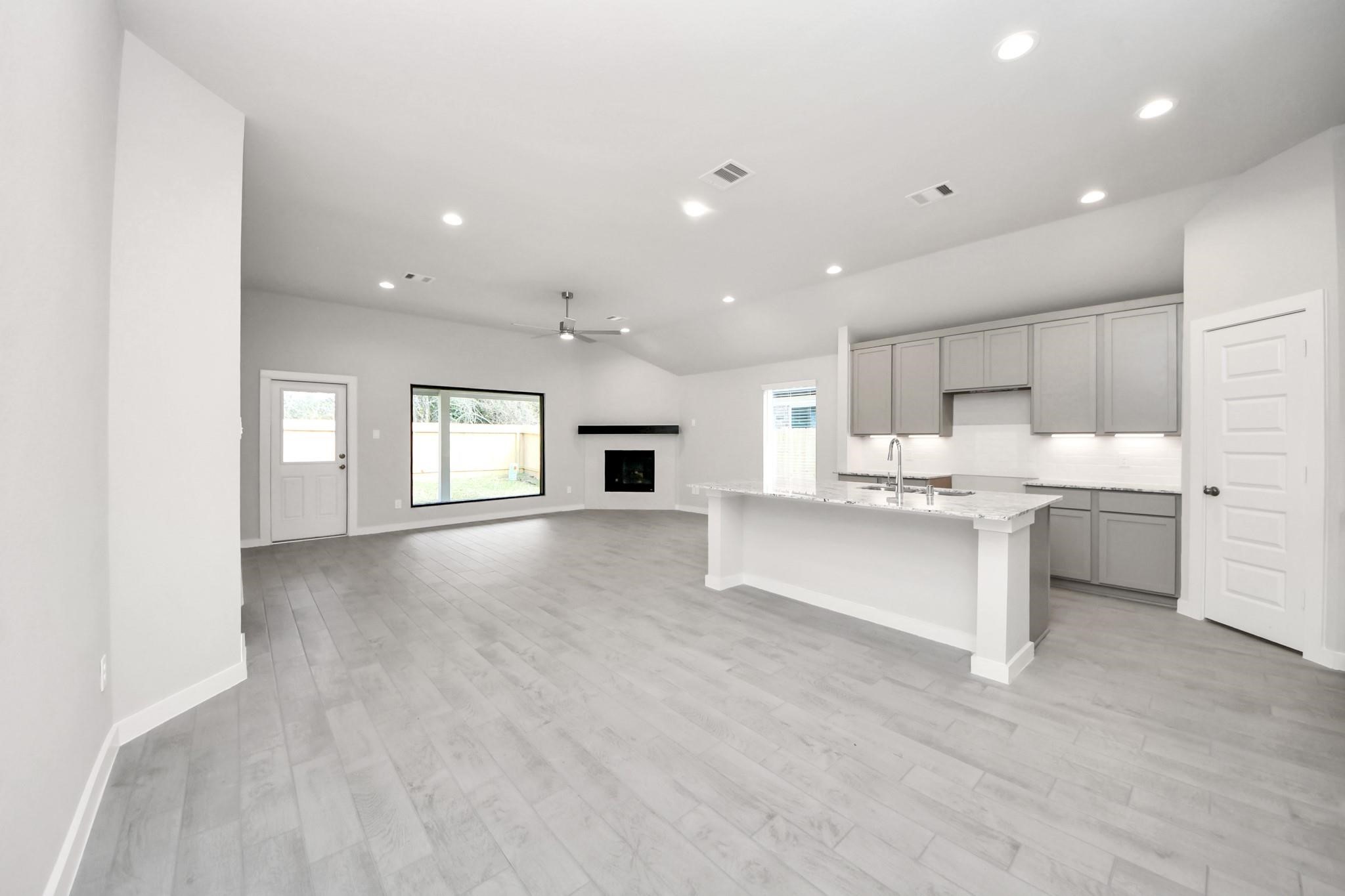 Spacious open-concept living area with sleek hardwood floors, modern kitchen featuring an island with bar seating, and a cozy fireplace under a vaulted ceiling. Spacious open-concept living area with sleek hardwood floors, modern kitchen featuring an island with bar seating, and a cozy fireplace under a vaulted ceiling.