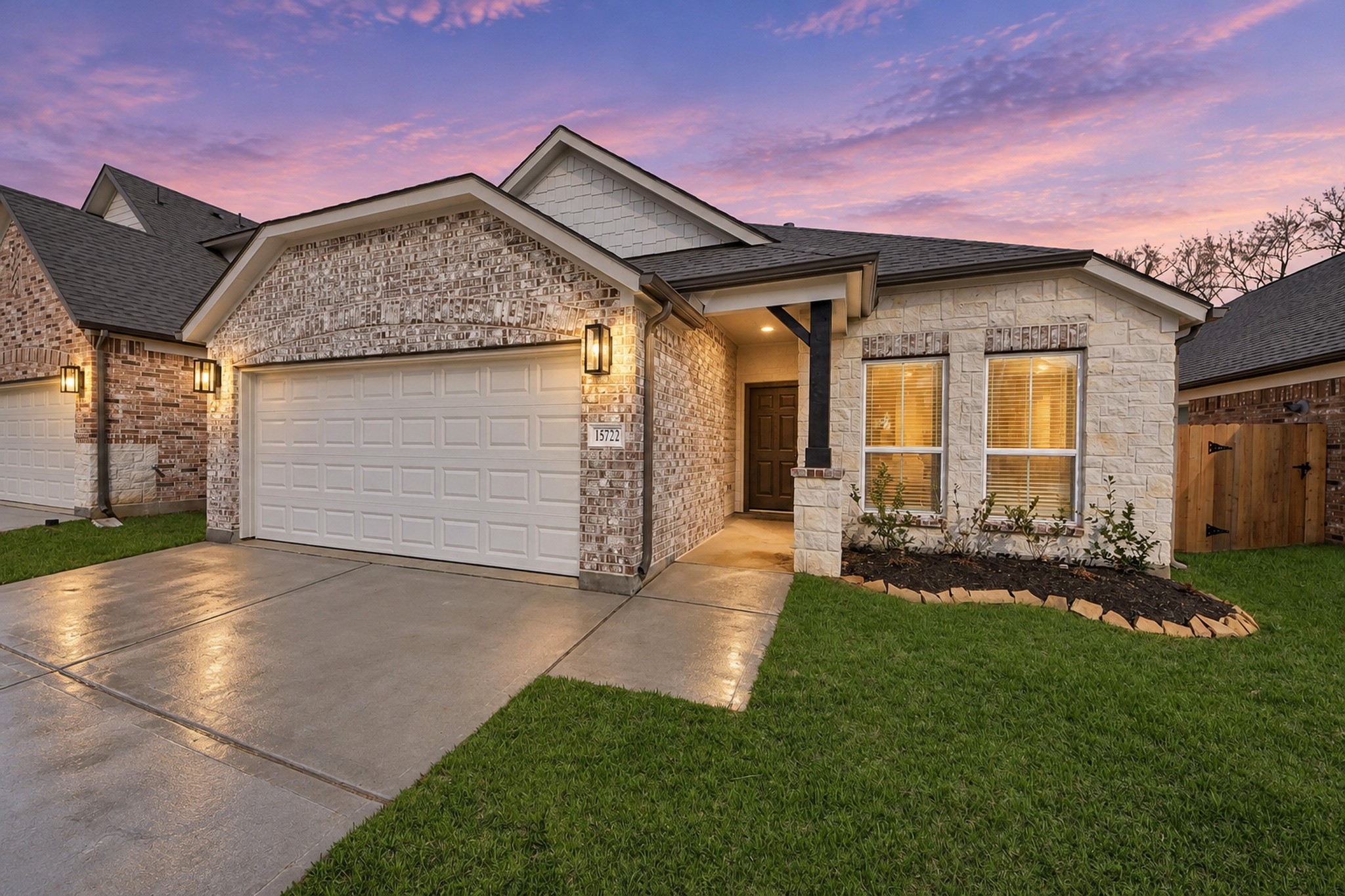 Charming brick home with a well-maintained lawn, featuring a spacious two-car garage and inviting entryway under a picturesque sunset sky.