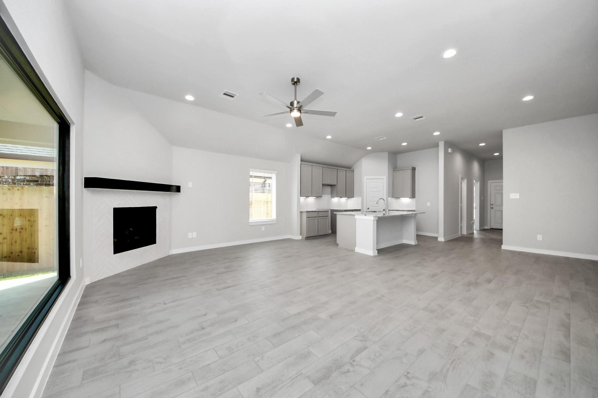 Spacious open-concept living area featuring sleek hardwood floors, a modern corner fireplace, and a bright kitchen with an island and ample cabinetry.