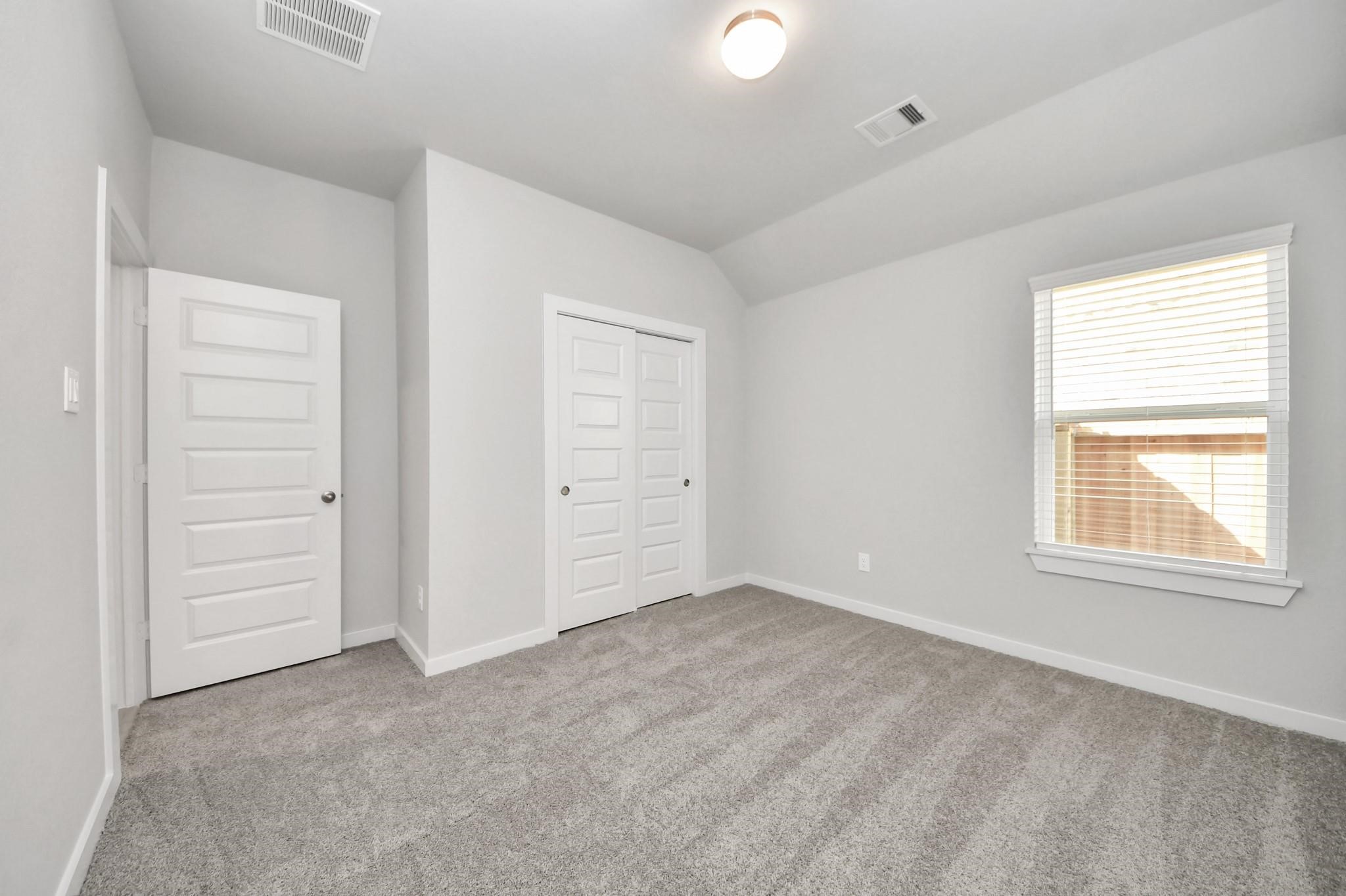 Bright and airy bedroom featuring plush carpeting, dual closet doors, and a large window for natural light.