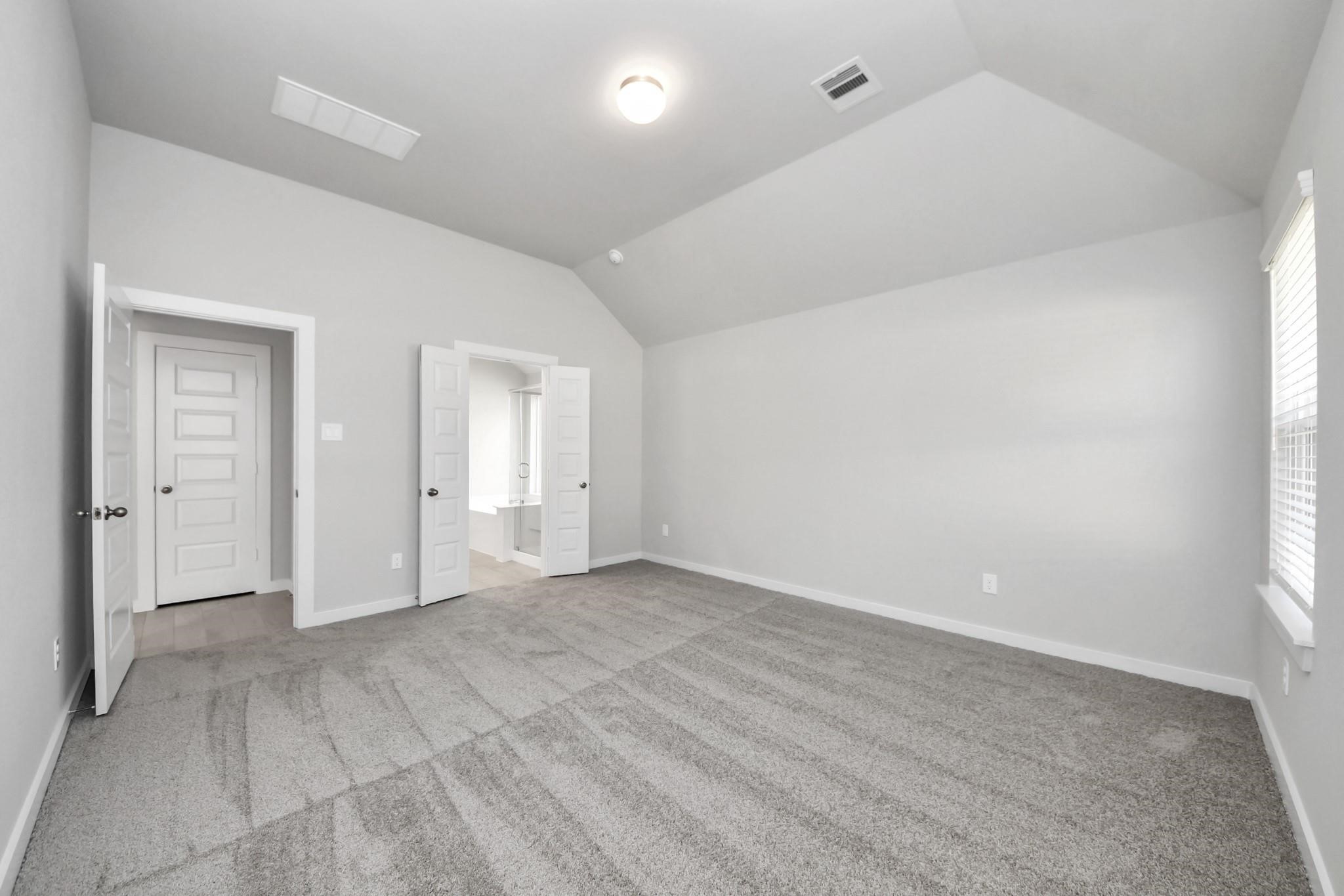 Spacious bedroom with vaulted ceilings, soft carpet flooring, and ample natural light from a large window, offering a serene retreat.