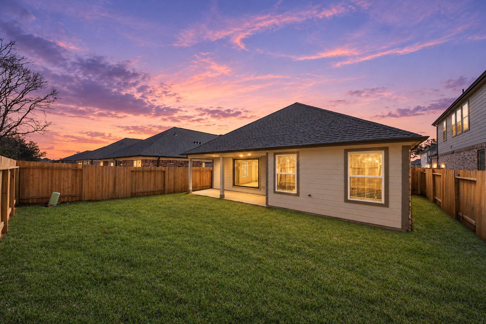 Charming backyard with lush green lawn and privacy fence, perfect for relaxing evenings under a stunning sunset sky.