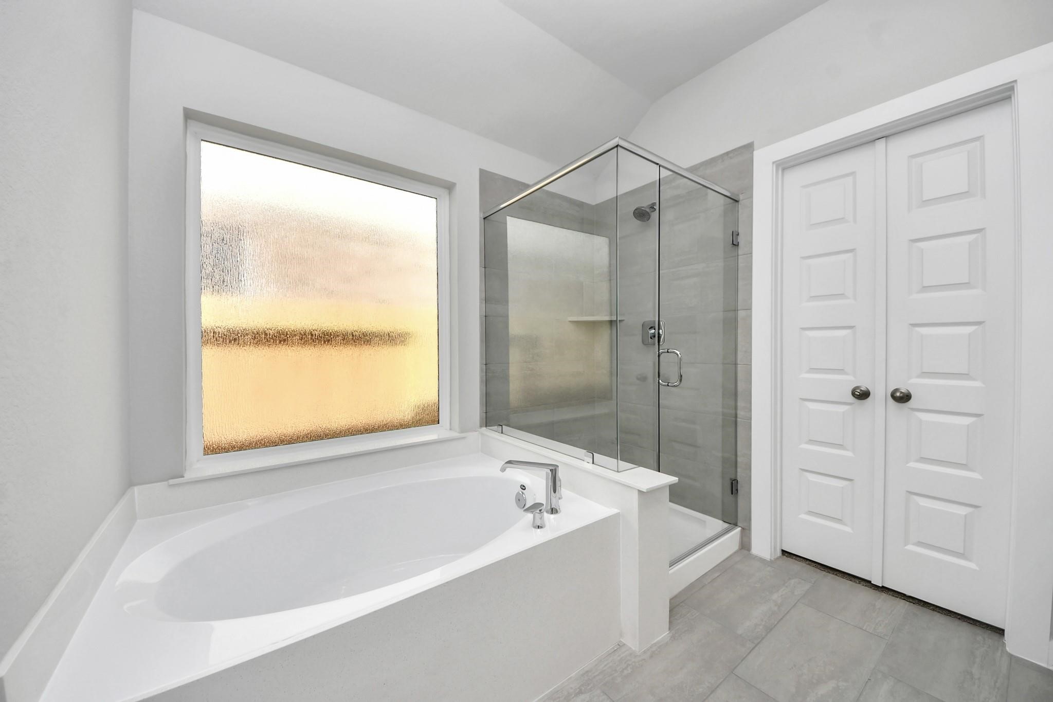 Bright and modern bathroom featuring a spacious soaking tub, a sleek glass-enclosed shower, and ample natural light from a frosted window.