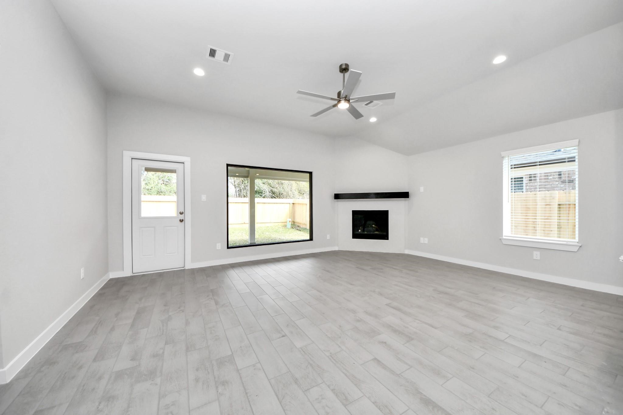 Spacious living room with modern gray flooring, a sleek corner fireplace, and large windows offering ample natural light. Spacious living room with modern gray flooring, a sleek corner fireplace, and large windows offering ample natural light.