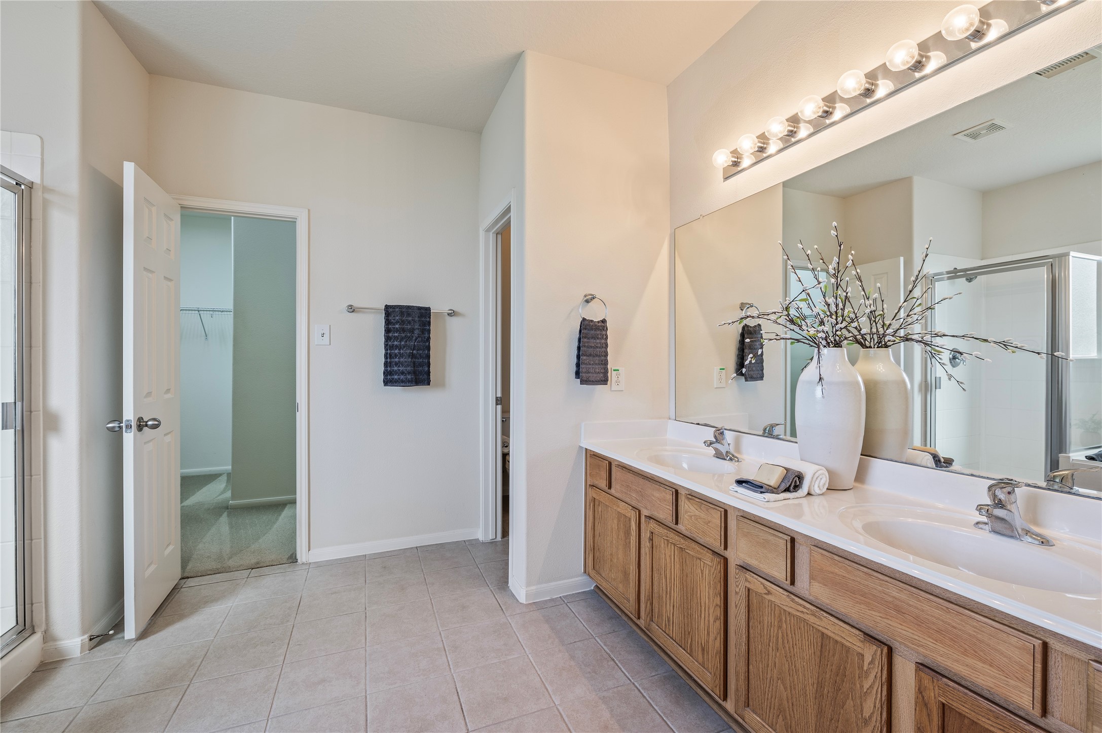 The primary bath offers double vanities, a large mirror, tile flooring and access to the walk-in closet.