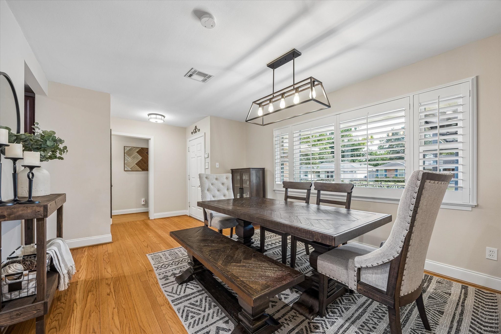 Front dining space offers flexibility for gathering without taking over the main living room. Wood floors continue toward the hallway, connecting the home's shared spaces with its bedroom wing.