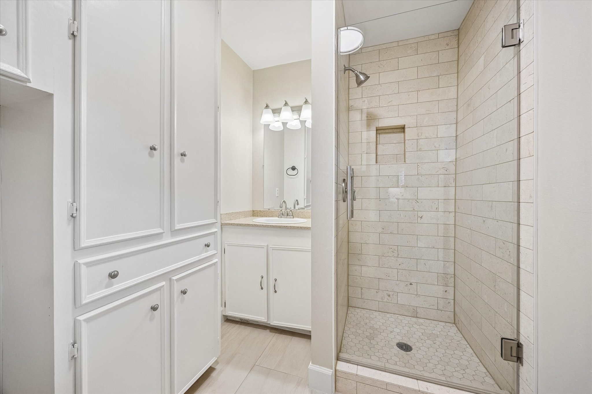 Glass enclosed shower features a recessed niche for bathing essentials, while tall cabinetry adds useful towel and linen storage. This full bath provides an additional bathing area separate from the bathroom near the bedrooms.