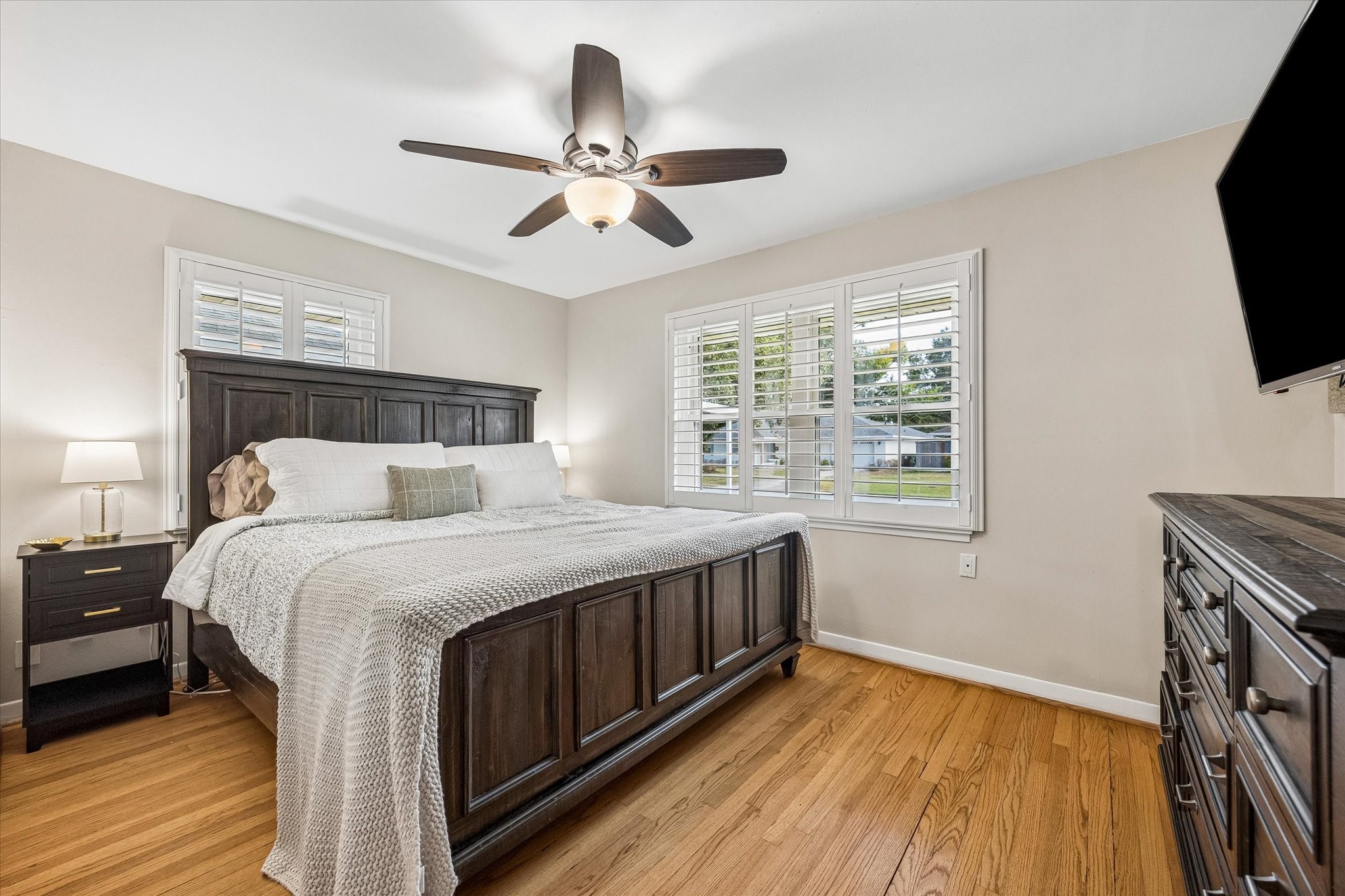 Windows on 2 sides bring natural light into this bedroom, complemented by wood floors and a ceiling fan. Located along the bedroom wing, the room offers a comfortable retreat from the home's main gathering areas.