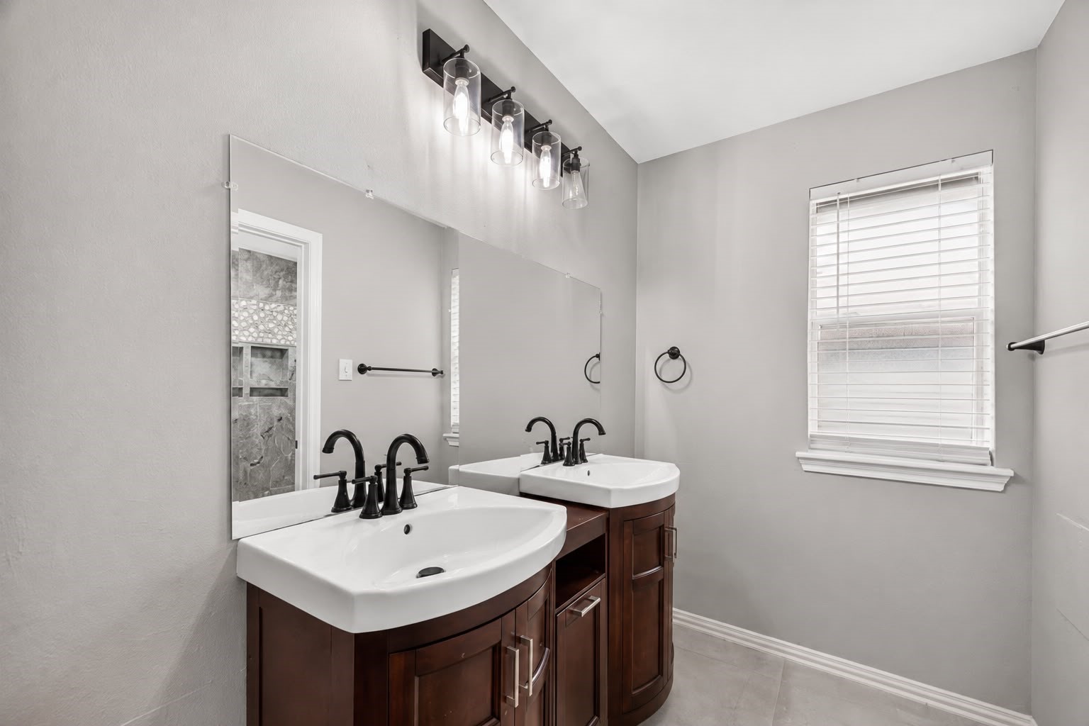 Modern bathroom featuring a double sink vanity with elegant dark wood cabinets, sleek fixtures, and a large mirror, complemented by a soft gray color palette and ample natural light.