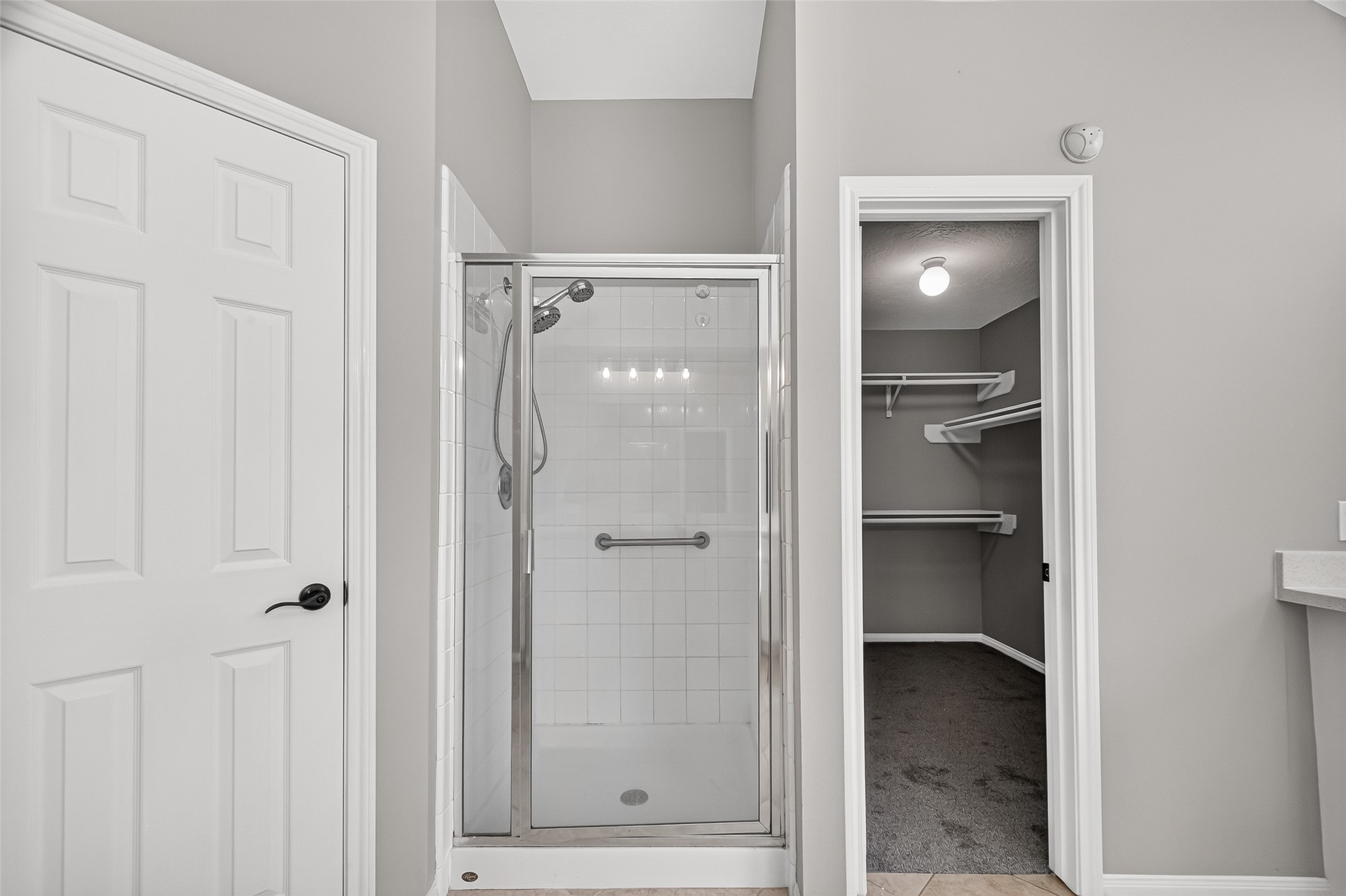 A sleek, modern bathroom features a glass-enclosed shower alongside a spacious walk-in closet with ample shelving, all set against elegant, neutral tones.