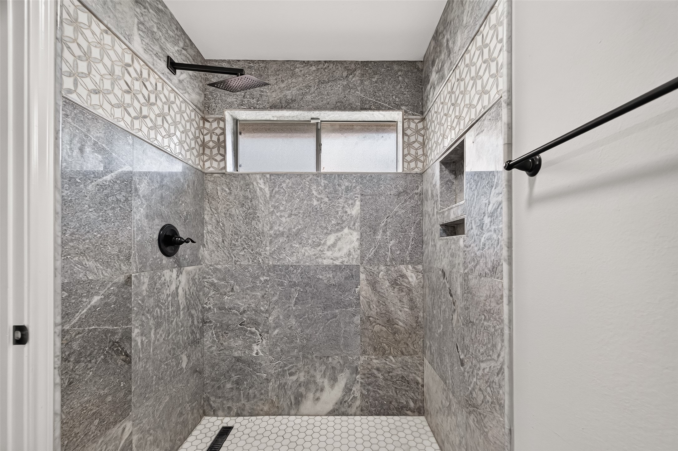 Luxurious bathroom featuring elegant gray marble tiles, a stylish geometric accent strip, and a modern rainfall showerhead for a spa-like experience.
