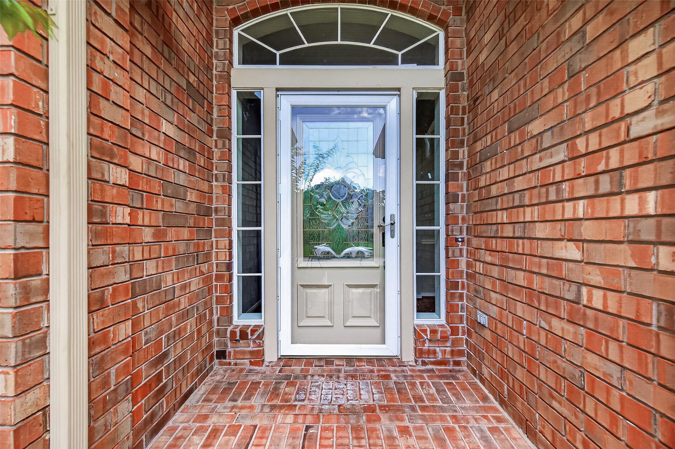 Charming brick entryway with a decorative glass front door and sidelights, offering a warm and inviting welcome.