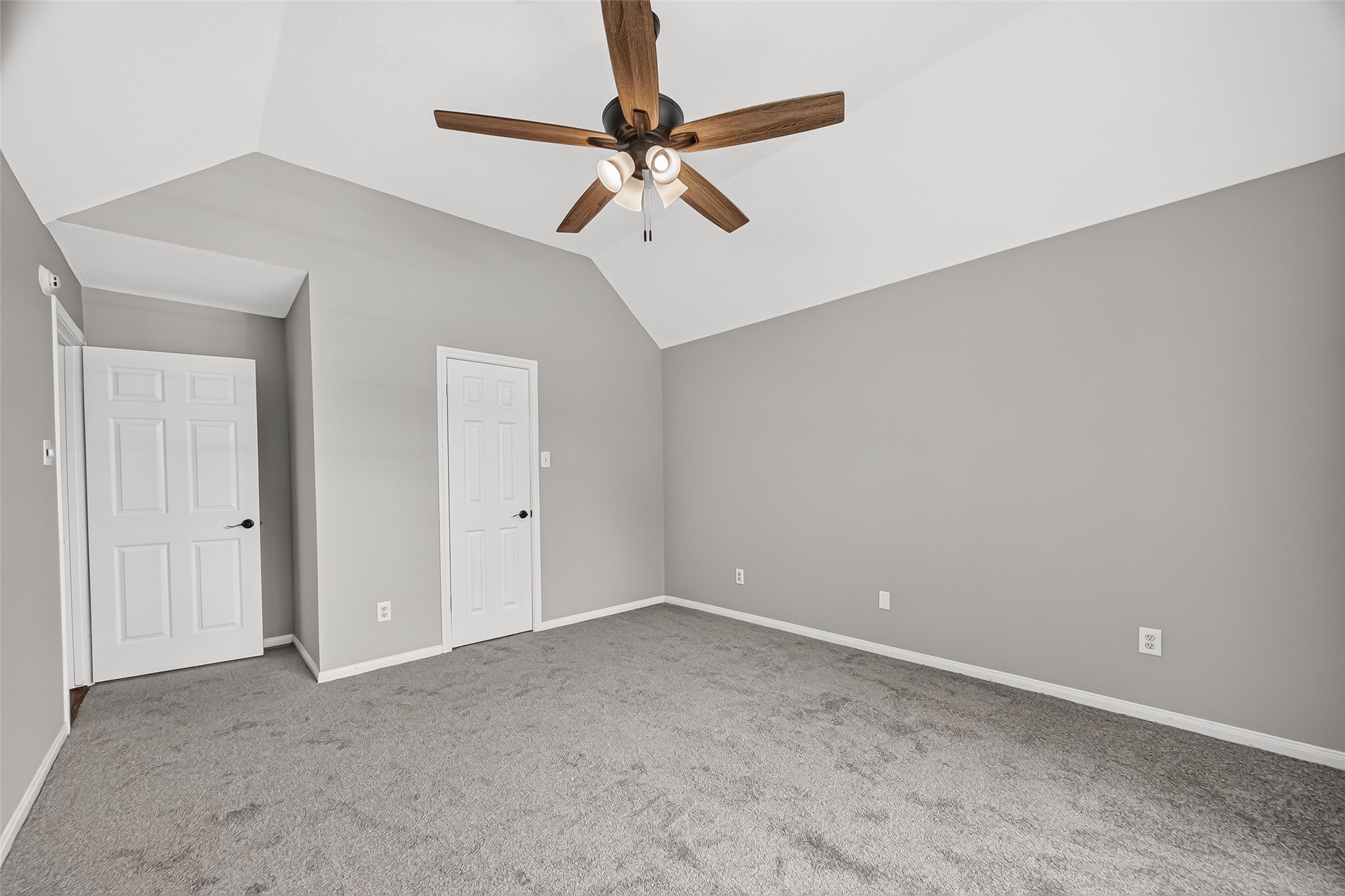 Spacious bedroom featuring a vaulted ceiling, modern ceiling fan, and plush carpeting, perfect for comfort and style.