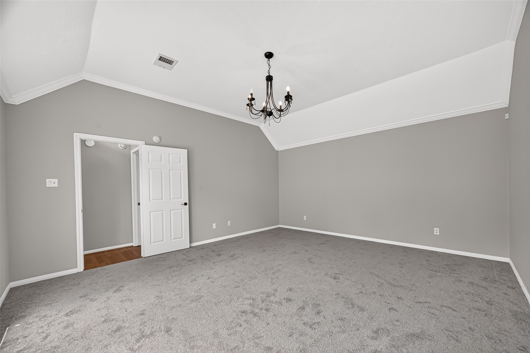Spacious bedroom with vaulted ceilings, elegant chandelier, and plush carpet, offering a serene and inviting atmosphere.