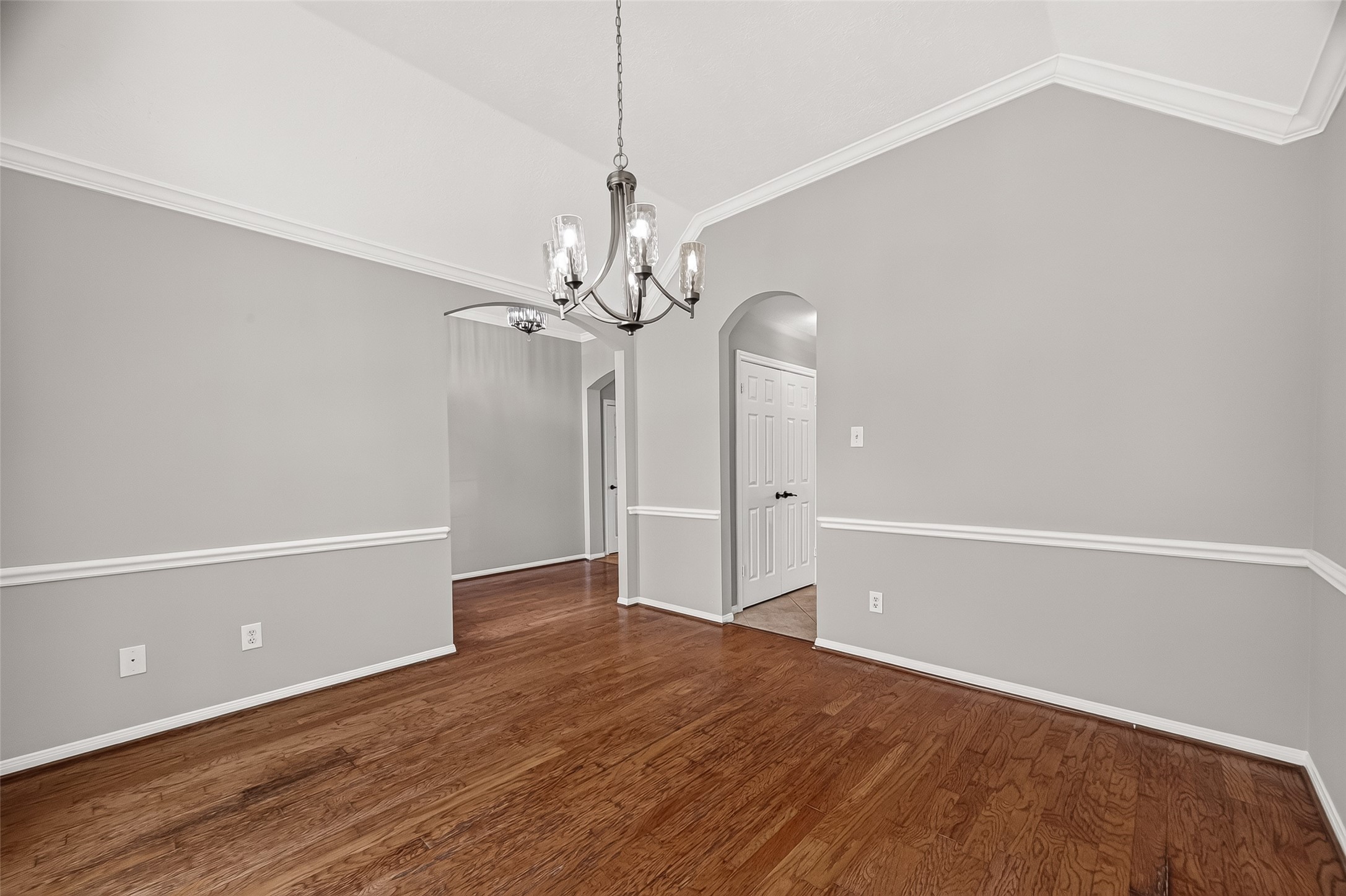 Elegant dining area with hardwood floors, a contemporary chandelier, and stylish wainscoting, creating a sophisticated space for entertaining.