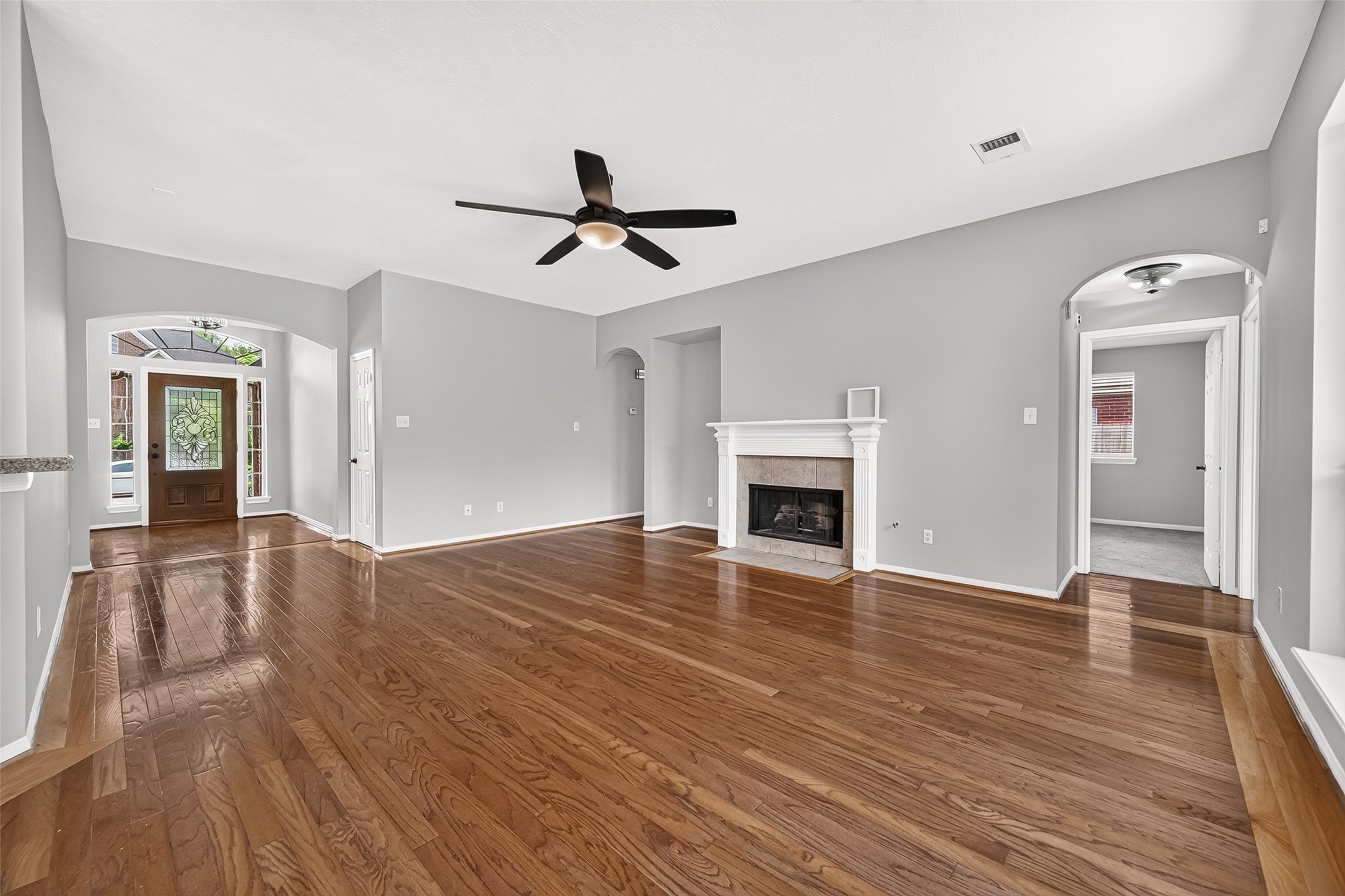 Spacious living room with gleaming hardwood floors, a cozy fireplace, and abundant natural light from large windows, perfect for relaxation and entertaining.