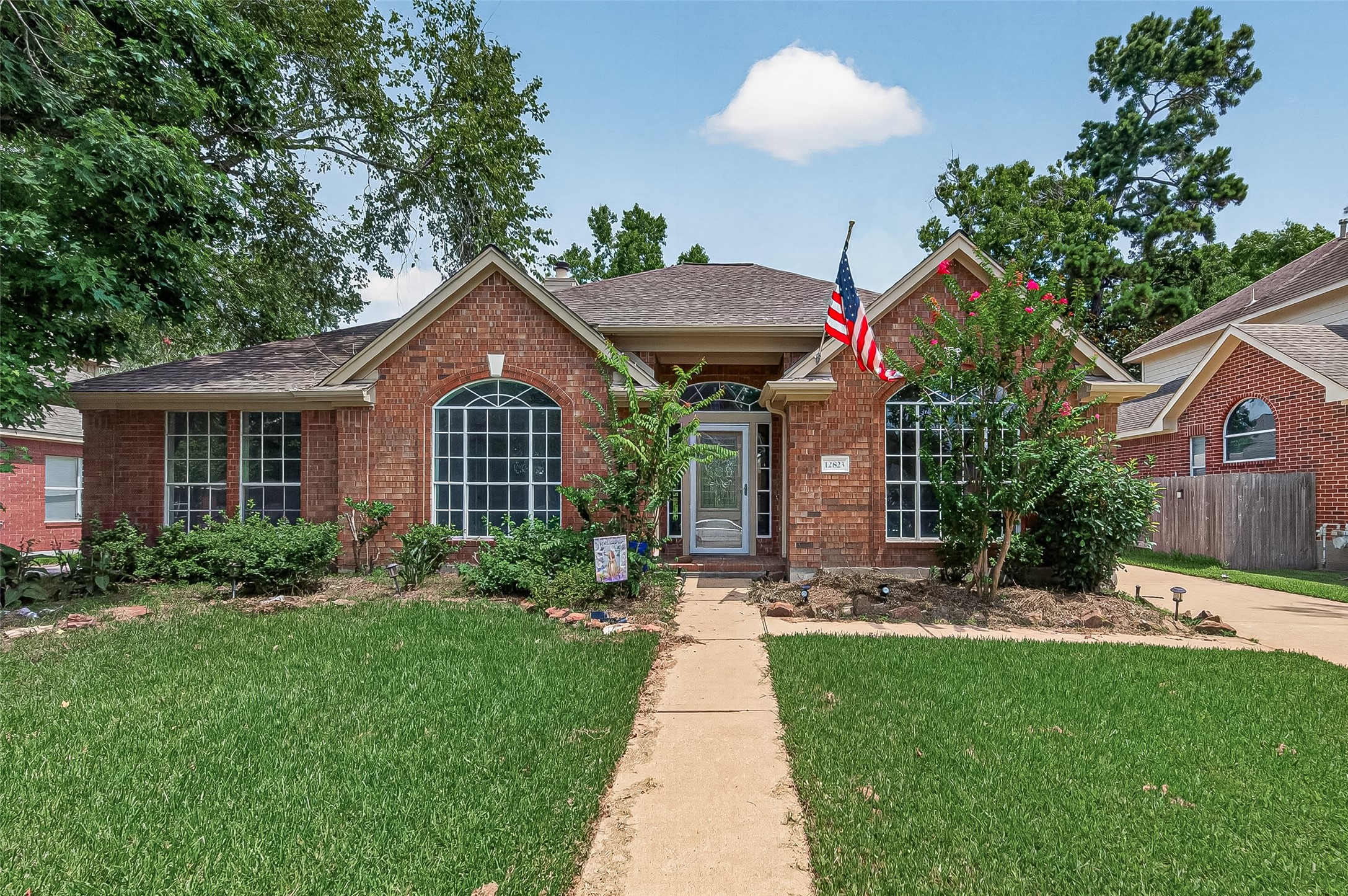 Charming brick home with a welcoming front entrance, large arched windows, and a well-maintained lawn. Located in a serene neighborhood with mature trees and a cozy front garden.