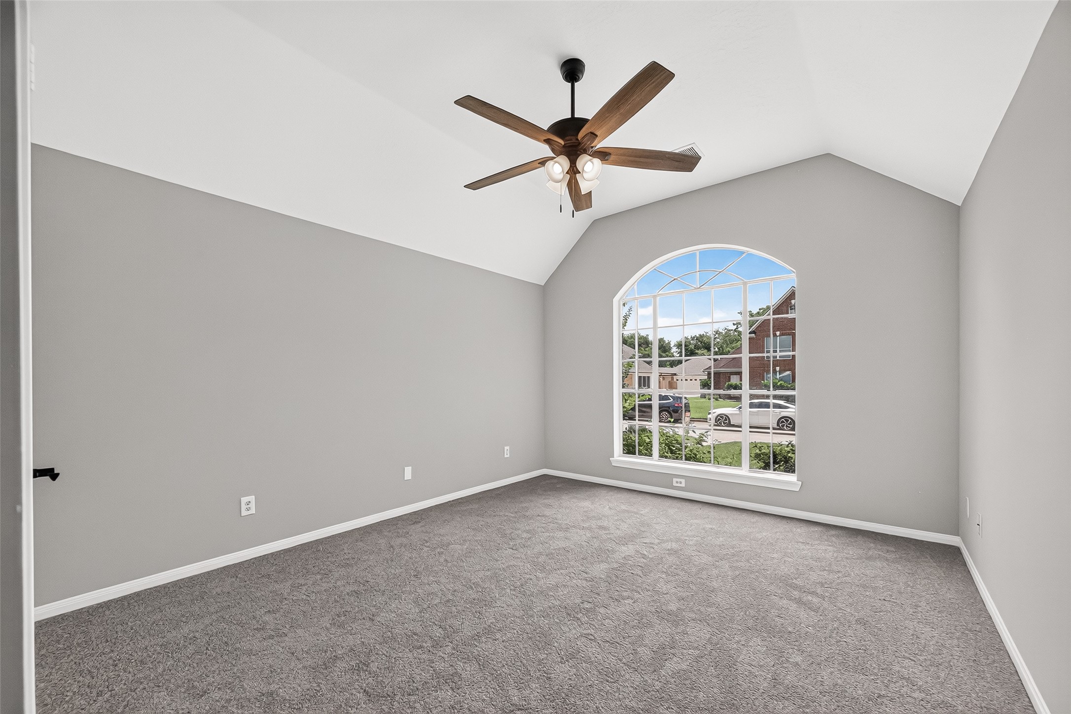 Spacious, light-filled room featuring a vaulted ceiling, elegant fan, and a large arched window overlooking the neighborhood.