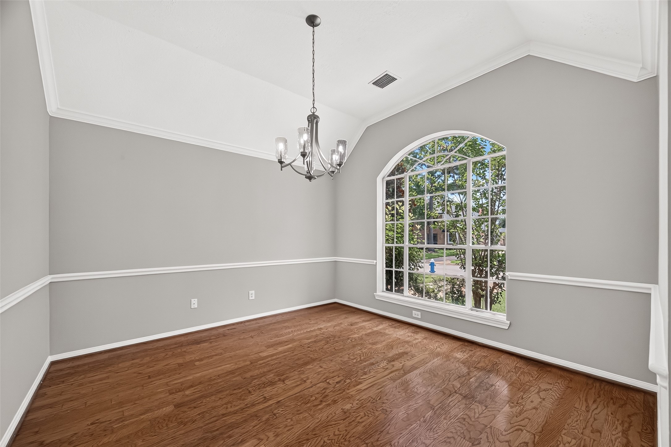 Elegant dining room featuring large arched windows that invite natural light, complemented by wood flooring and a stylish chandelier.