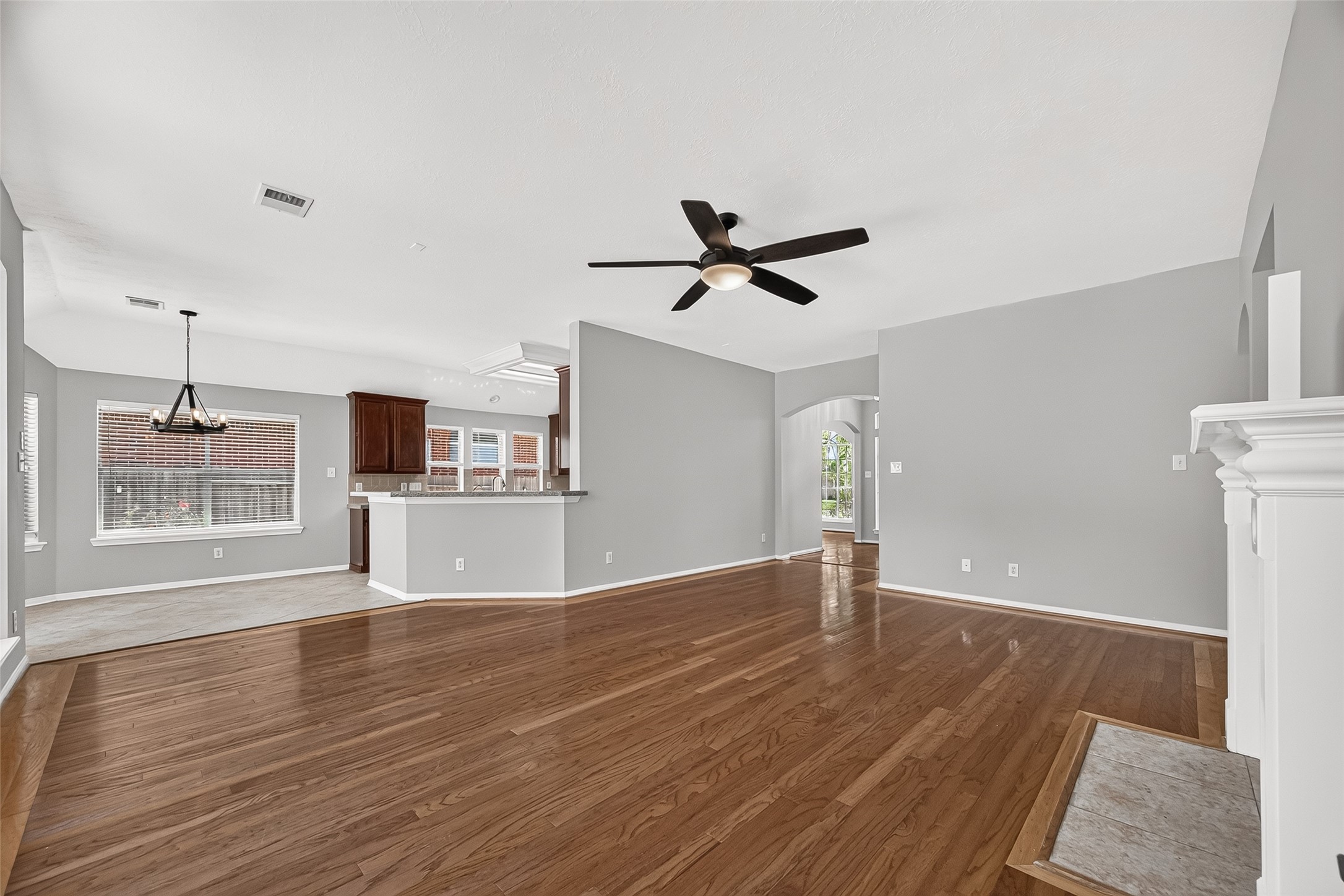 Spacious open-concept living area with sleek hardwood floors, modern ceiling fan, and abundant natural light, seamlessly connecting to a bright kitchen and dining space.
