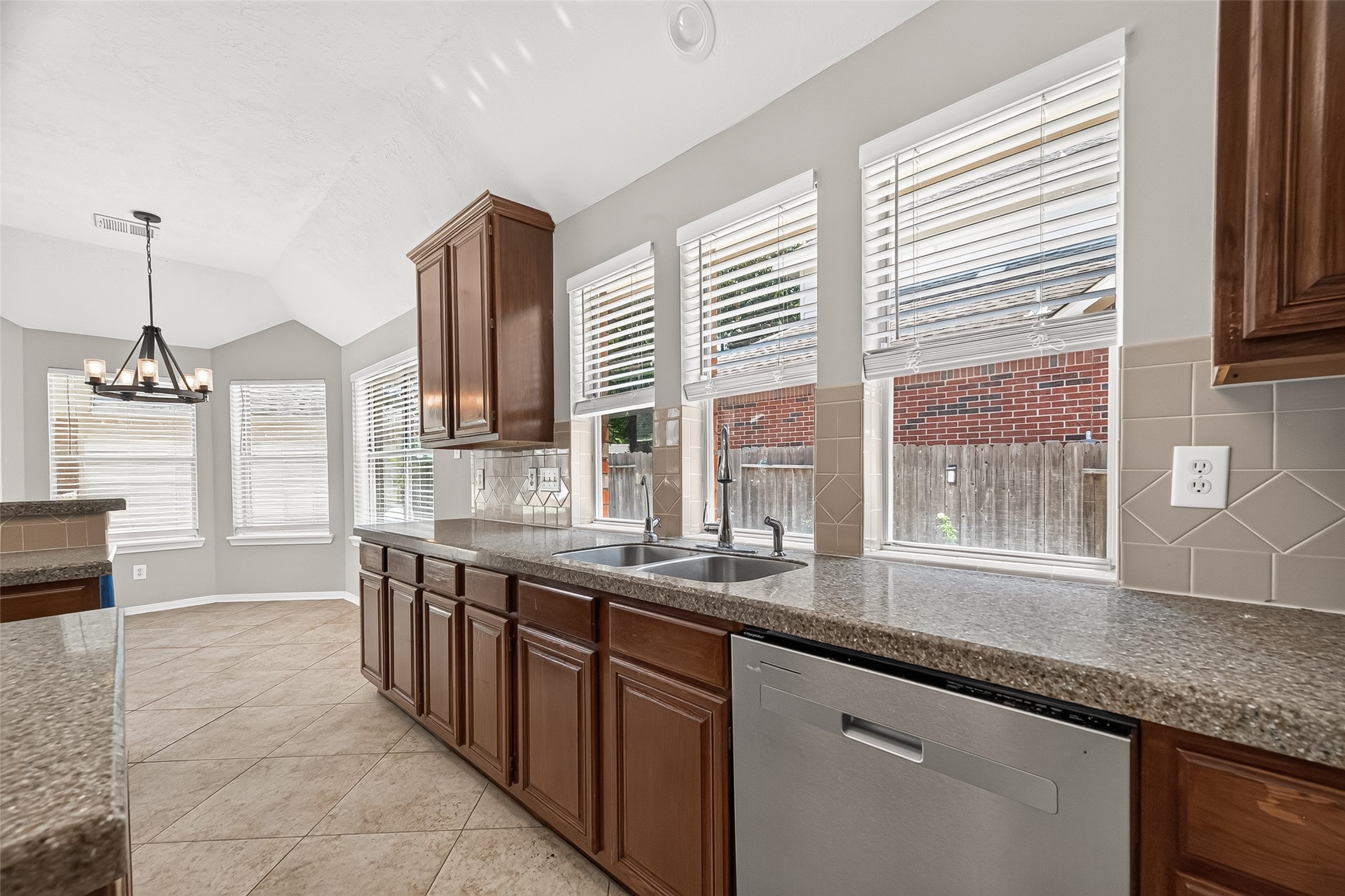 Bright kitchen featuring expansive windows, modern stainless steel fixtures, and rich wood cabinetry. The tiled backsplash and spacious countertops offer style and functionality, perfect for meal prep and entertaining.