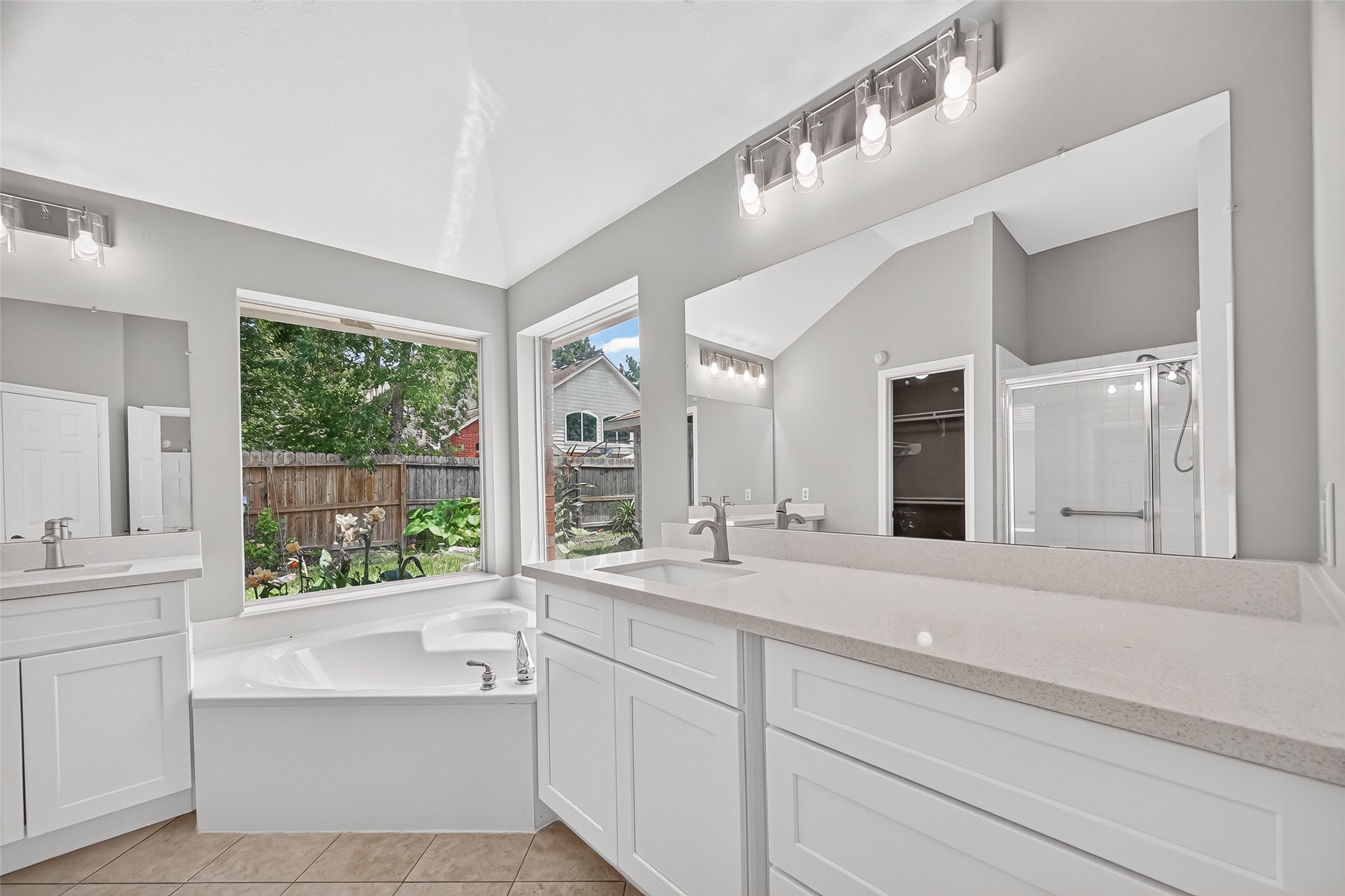 Bright and spacious bathroom featuring double vanities with sleek countertops, a luxurious corner bathtub, and a separate glass-enclosed shower, all enhanced by large windows providing ample natural light.