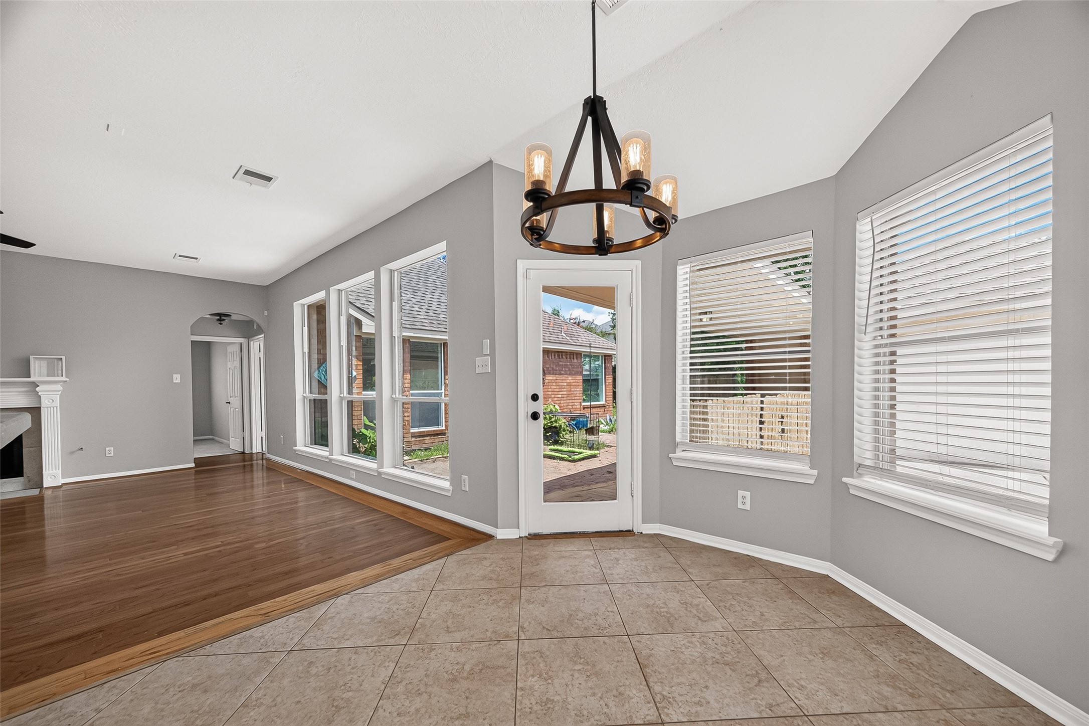 Bright dining area with large windows, stylish chandelier, and easy access to the outdoor space, seamlessly connecting to a spacious living room with elegant wood flooring and a cozy fireplace.