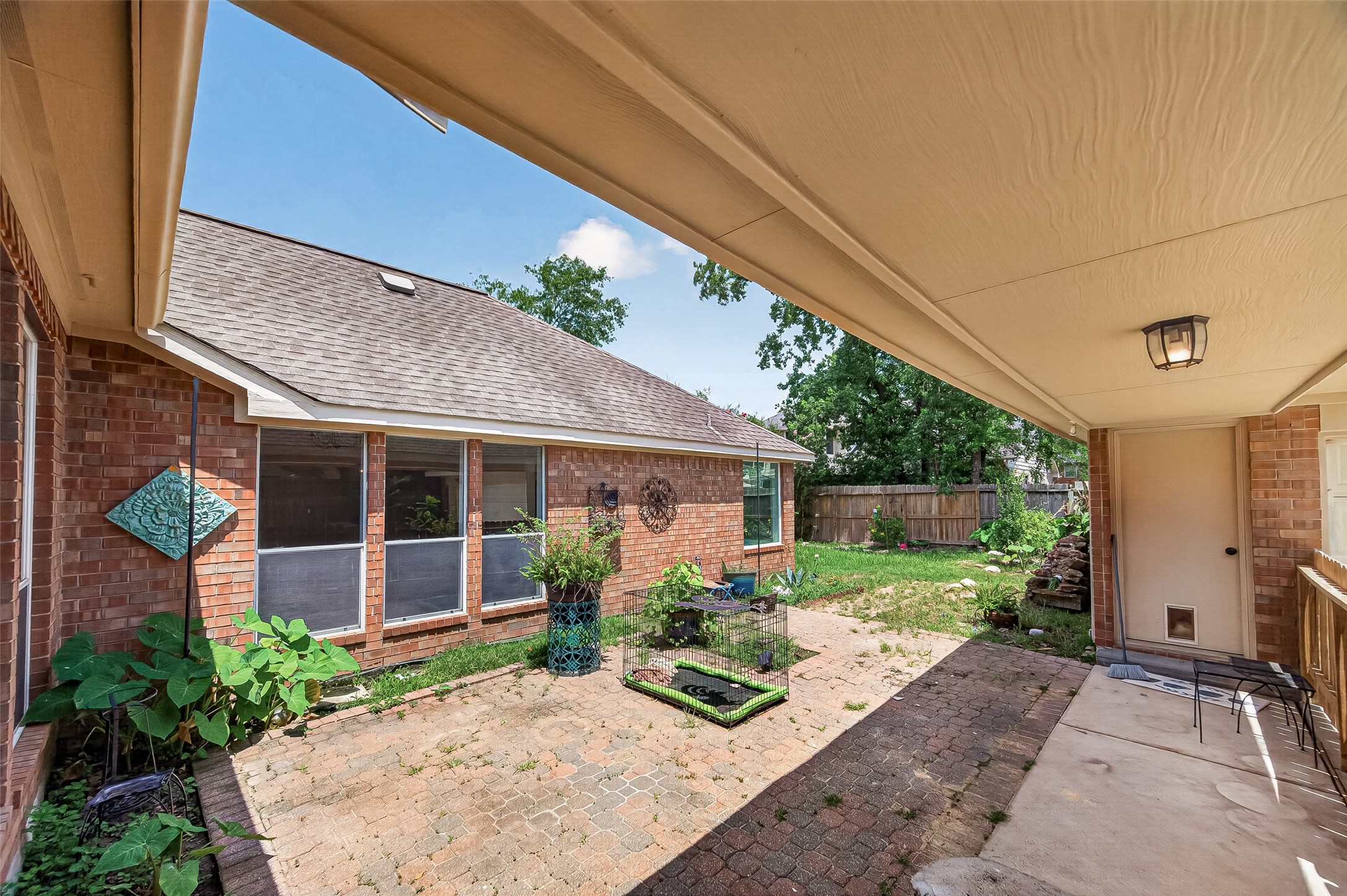 Backyard patio with a mix of brick and stone paving, surrounded by lush greenery and a privacy fence, perfect for outdoor relaxation and entertaining.