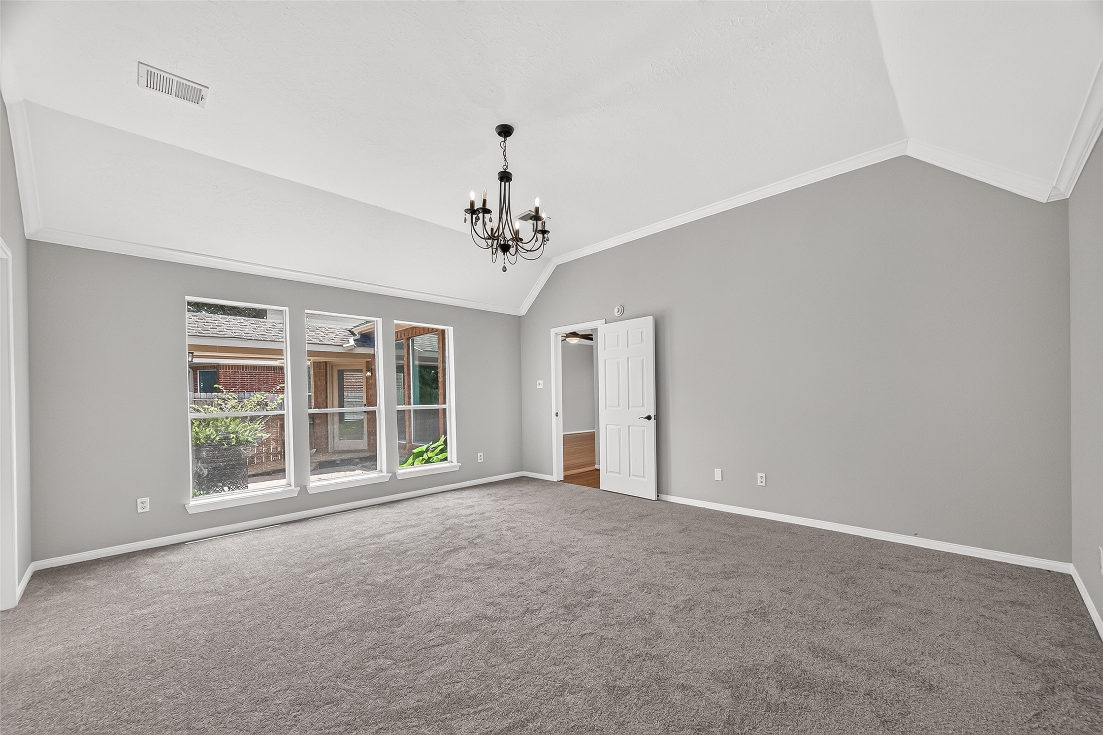 Spacious, light-filled room with elegant tray ceiling, plush carpeting, and a charming chandelier, offering a versatile space for relaxation or entertainment.