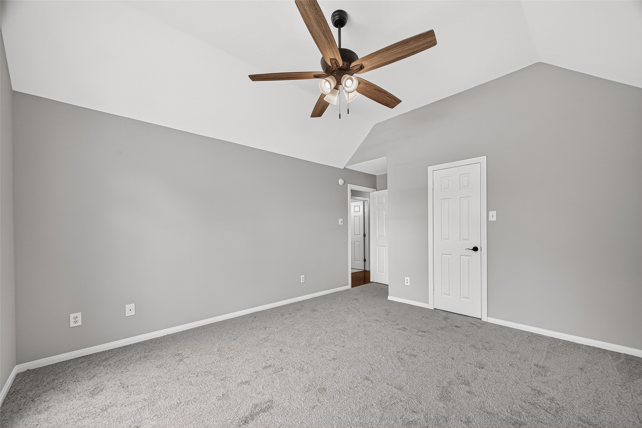 Spacious bedroom with soft gray walls, plush carpeting, and a stylish ceiling fan, offering a tranquil retreat.