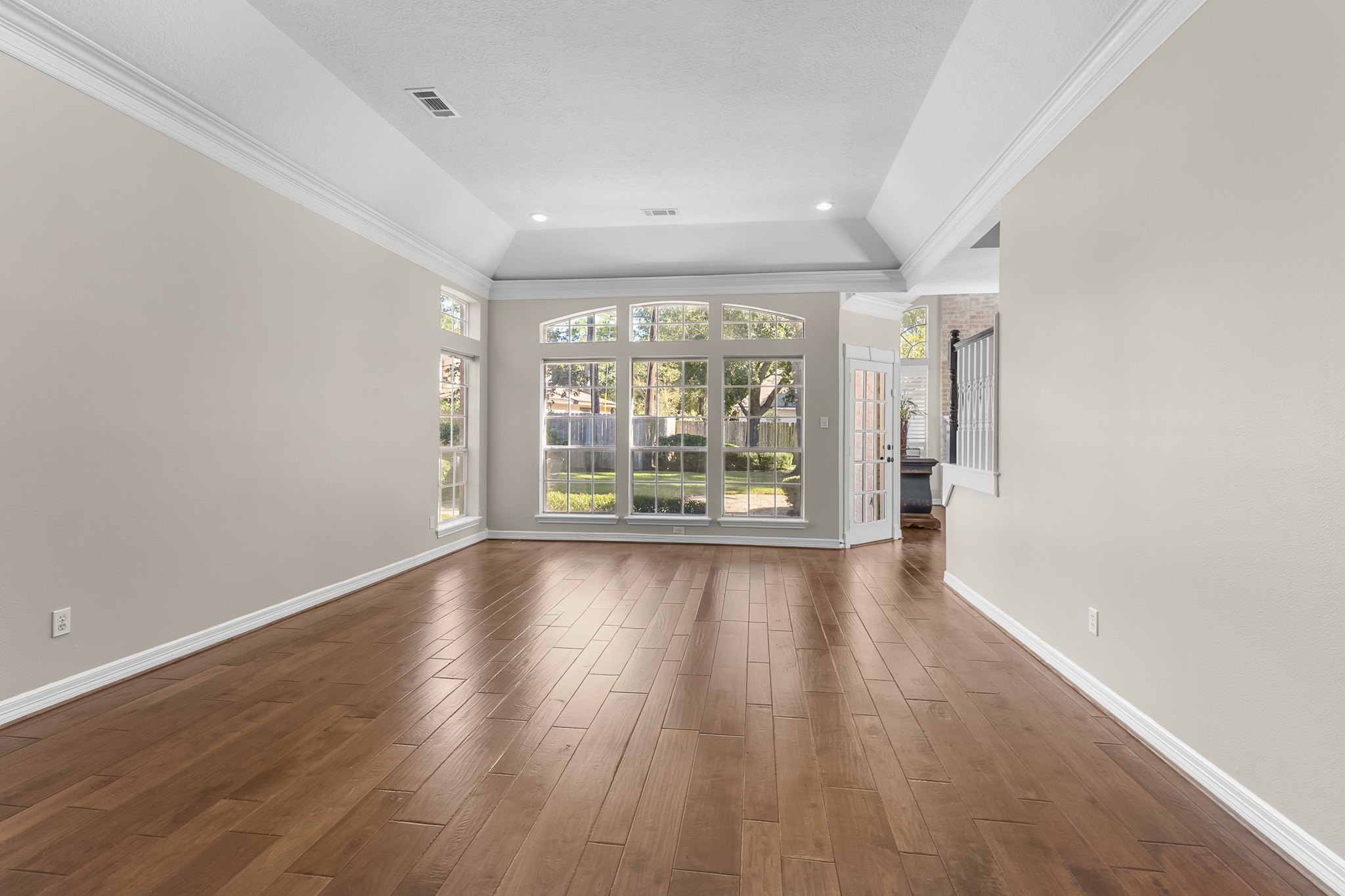 A broad expanse of windows brings natural light into this spacious living area, complemented by warm wood flooring and a detailed ceiling.