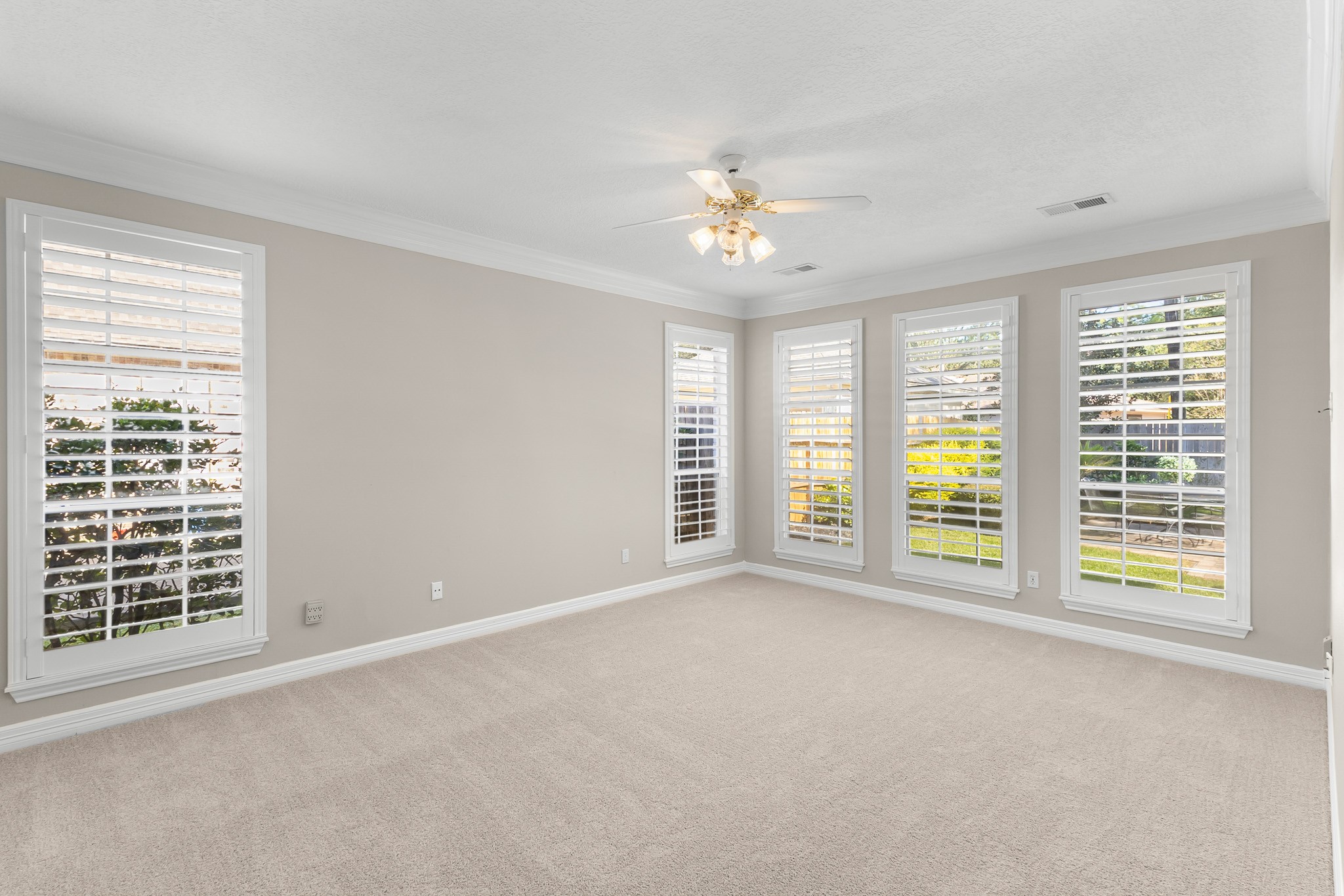 A spacious first-floor bedroom features soft neutral finishes, plantation shutters and abundant windows for a serene retreat.
