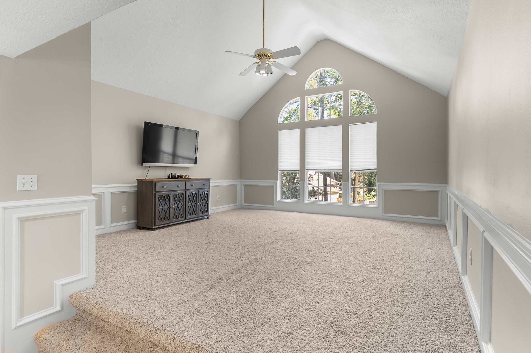 An expansive game room features a vaulted ceiling, decorative wall paneling and a dramatic arched window, offering space for recreation and relaxation.
