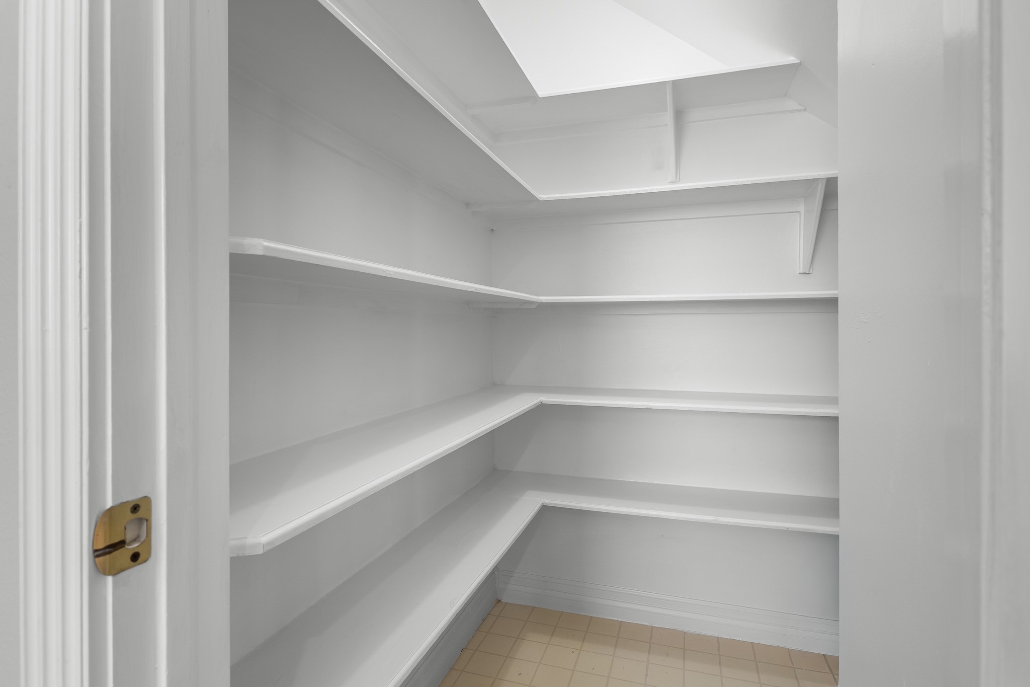 A spacious walk-in pantry with wraparound shelving offers plentiful room for dry goods, serving pieces and kitchen essentials.