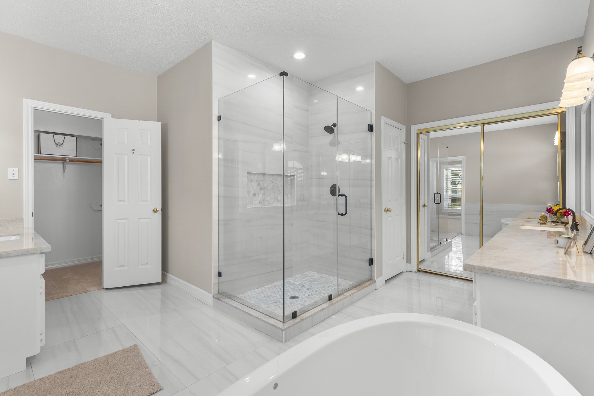 A glass-enclosed shower and separate soaking tub create a polished bathing space, complemented by bright finishes and generous natural light.